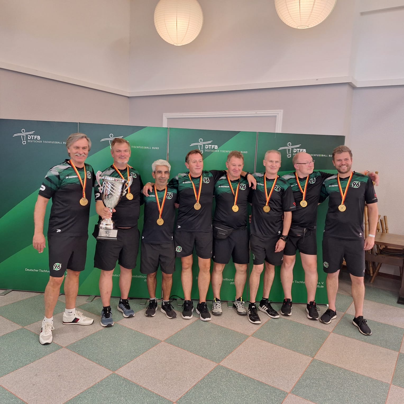 Die Tischfußballer lächeln in die Kamera und tragen dabei ihre Goldmedaille sowie den Pokal.