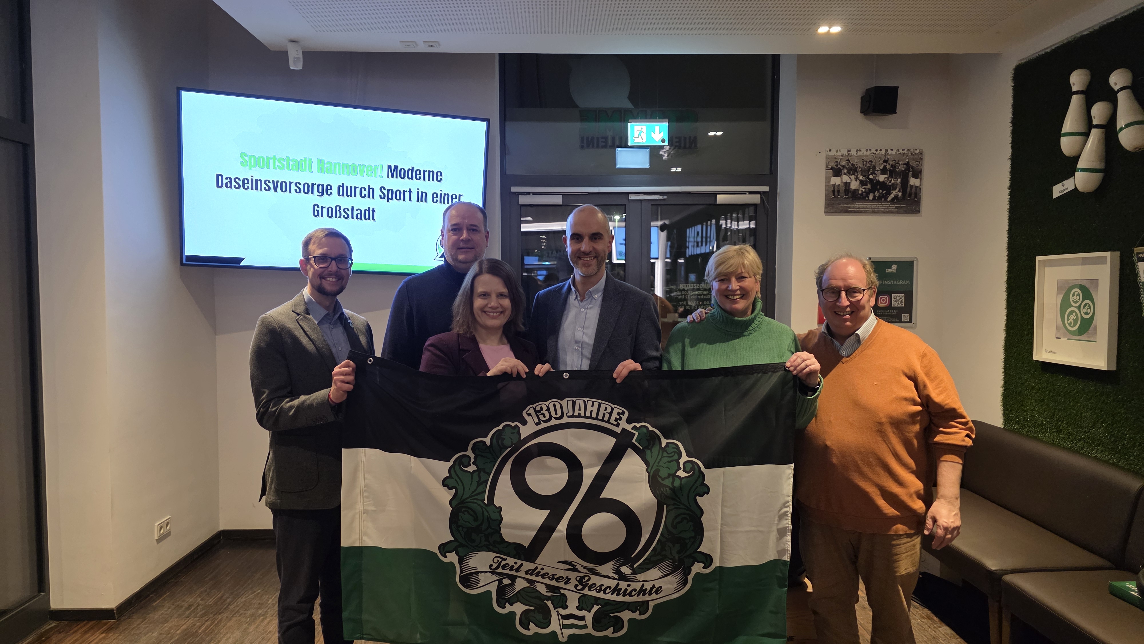 Alle Gäste der Veranstaltung stehen zusammen für ein Gruppenfoto mit einer 96-Fahne.