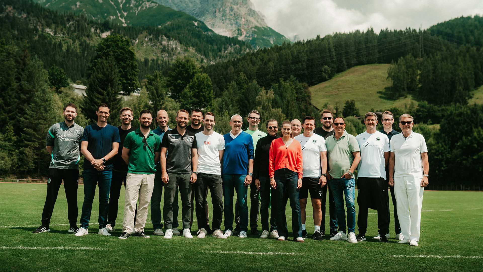 Die Verantwortlichen der 96-Partner stehen gemeinsam mit Verantwortlichen von Hannover 96 vor dem Bergpanorama in Saalfelden.