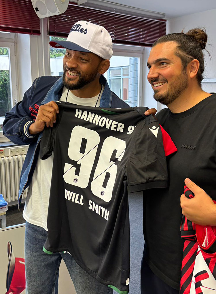 Will Smith hält das Hannover-96-Auswärtstrikot mit dem Flock Hannover 96 und Will Smith, neben ihm steht Hannover-Concerts-Geschäftsführer Nico Röger.  