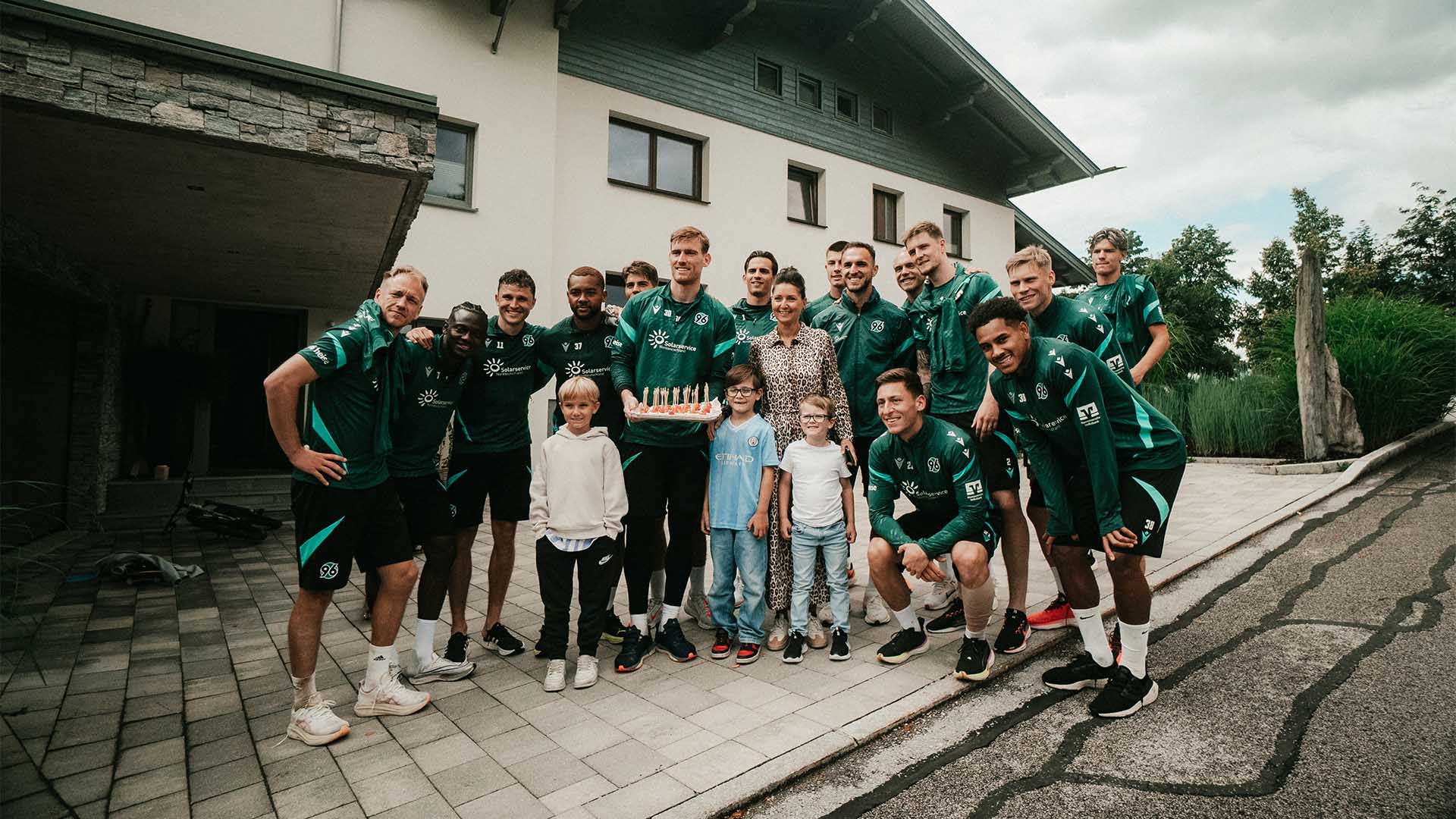 Einige 96-Spieler posieren mit einer Anwohnerin und drei Kindern sowie einem geschenkten Kuchen, den Leo Weinkauf hält. 