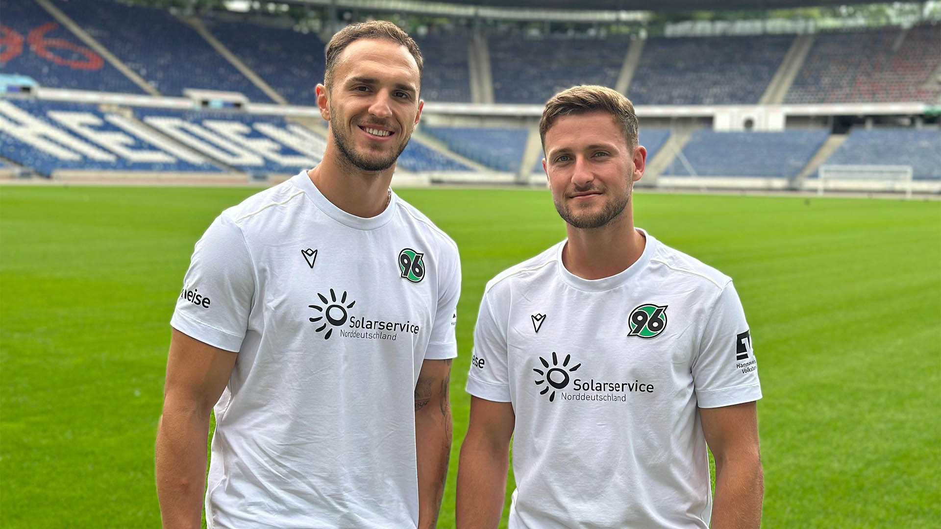 Virgil Ghita und Enzo Leopold stehen in der leeren Heinz von Heiden Arena und lächeln in die Kamera.