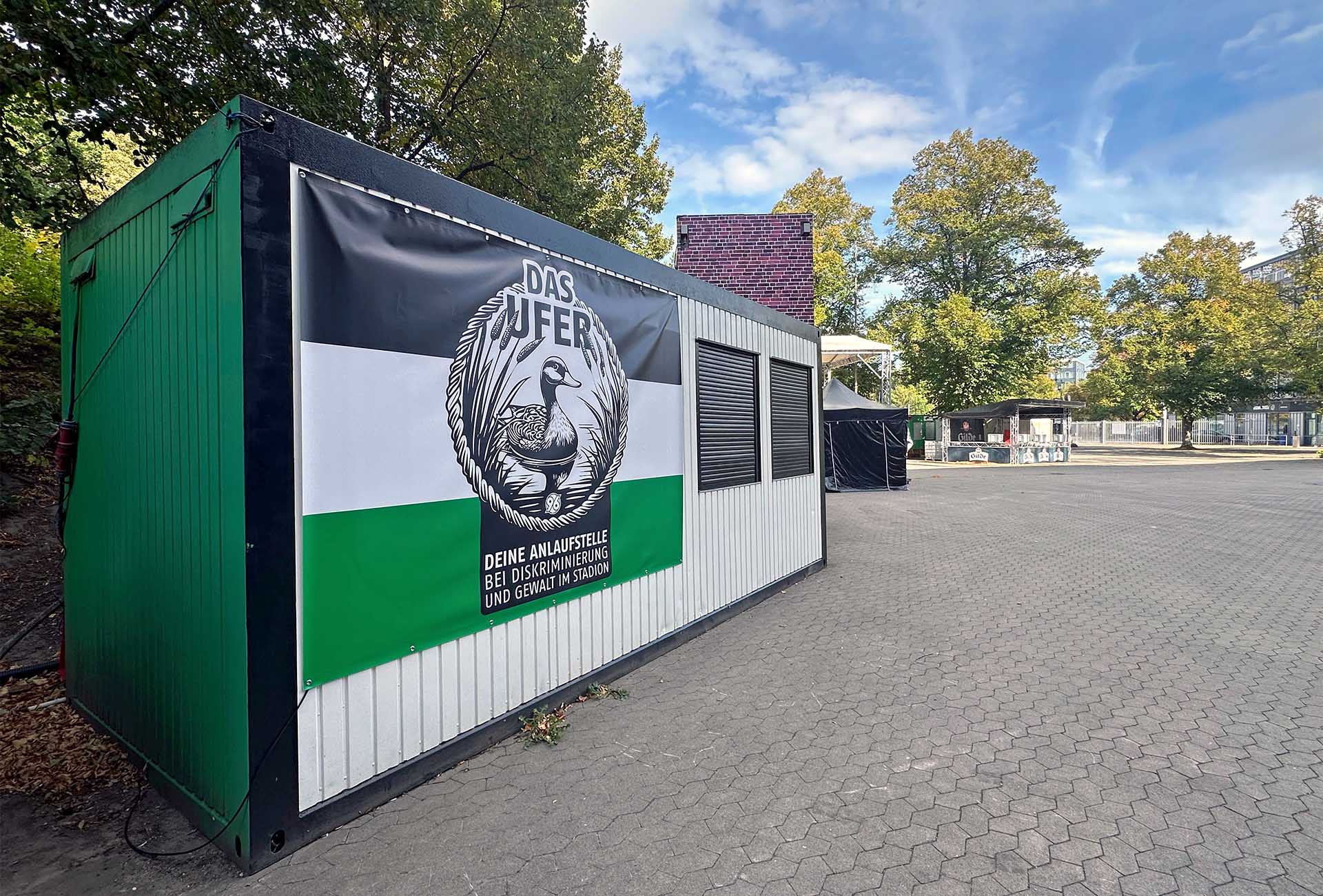 Der schwarz-weiß-grüne Container der Anlaufstelle mit dem Logo von "Das Ufer" mit einer Ente.