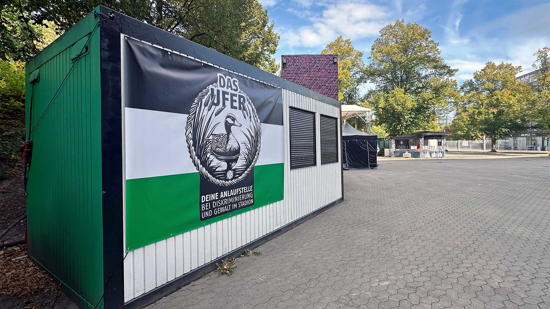Der schwarz-weiß-grüne Container der Anlaufstelle mit dem Logo von "Das Ufer" mit einer Ente.