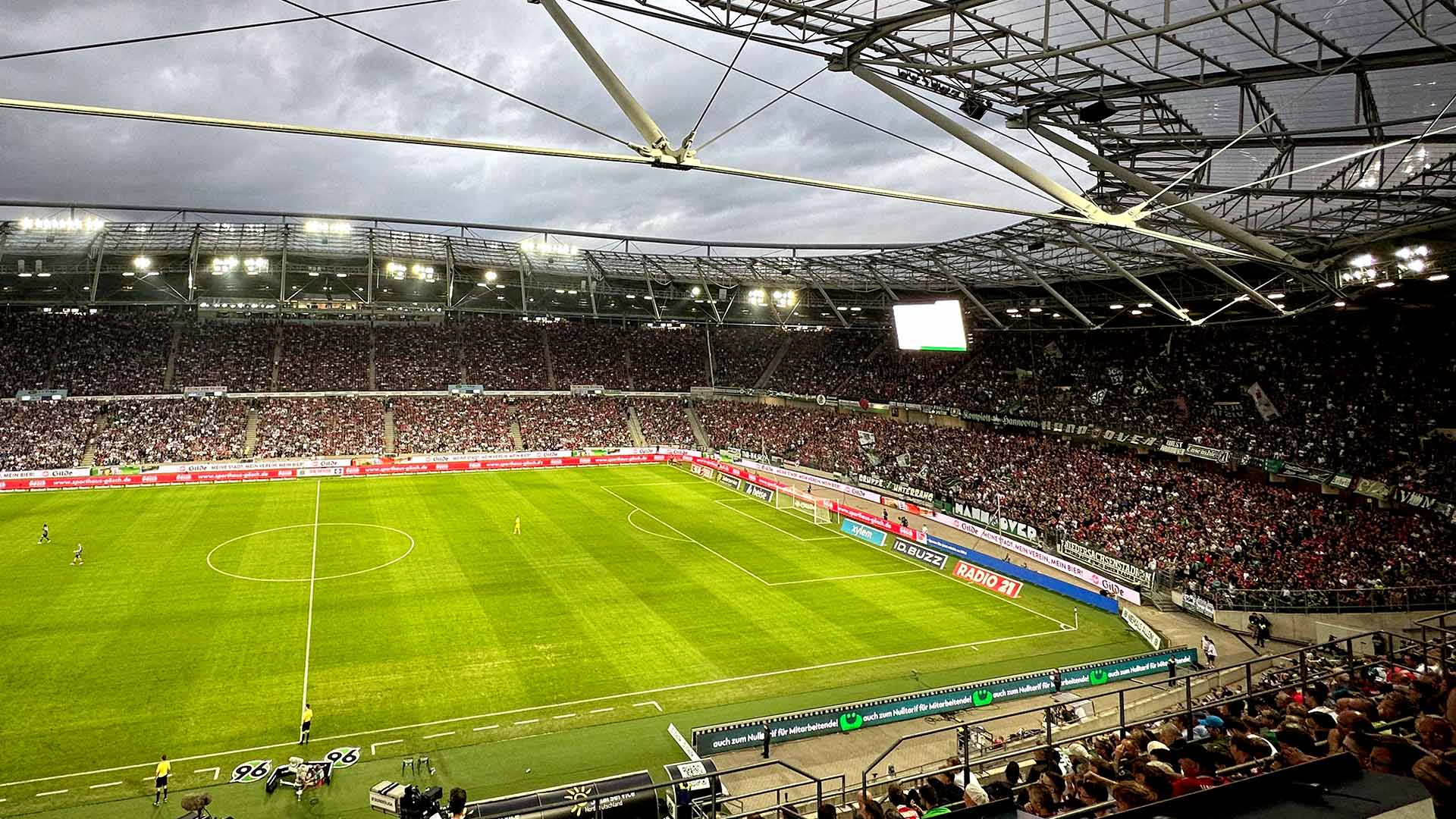 Die volle Nordkurve und ein Teil der Westkurve der Heinz von Heiden Arena bei Dämmerung und Flutlicht. 