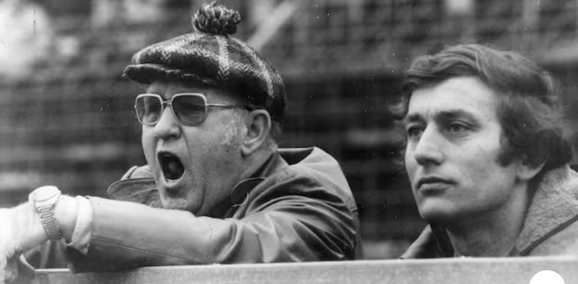 Zwei Personen stehen hinter einer Bande.