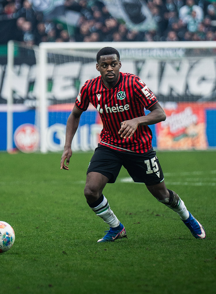 Noel Aseko am Ball, im Hintergrund 96-Fans. 