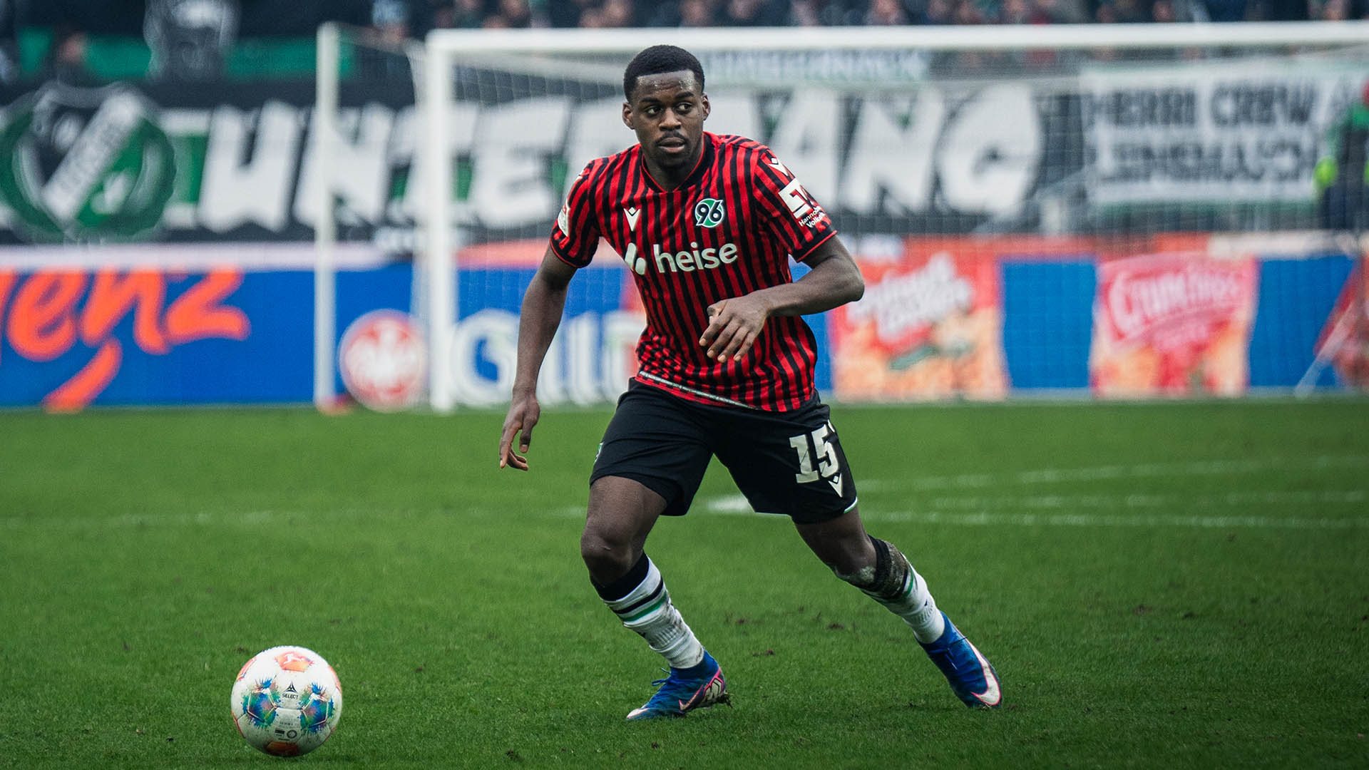 Noel Aseko am Ball, im Hintergrund 96-Fans. 