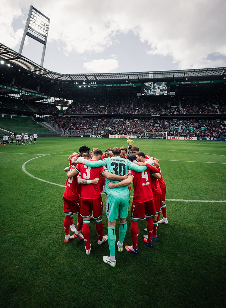 Die 96-Mannschaft steht in einem Kreis auf dem Rasen im Weserstadion, im Hintergrund die 96-Fankurve.