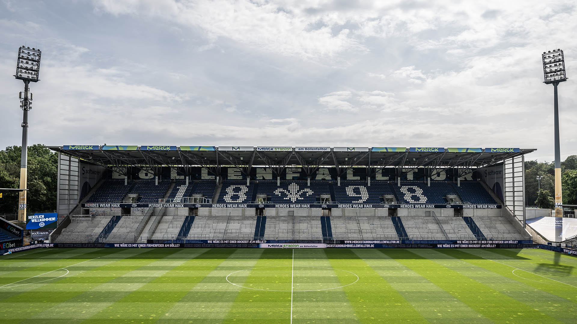 Blick auf die leere Tribüne im Stadion des SV Darmstadt 98. In den überwiegend blauen Sitzen bilden weiße Sitze das Lilien-Symbol und die Zahl 1898.