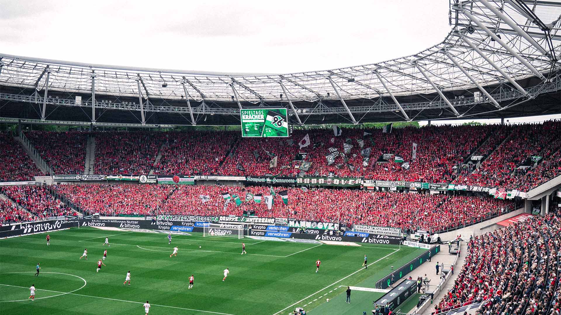 Blick in Richtung Nordkurve im vollen Stadion, die meisten Fans tragen rote Sachen, es läuft gerade ein Spiel.