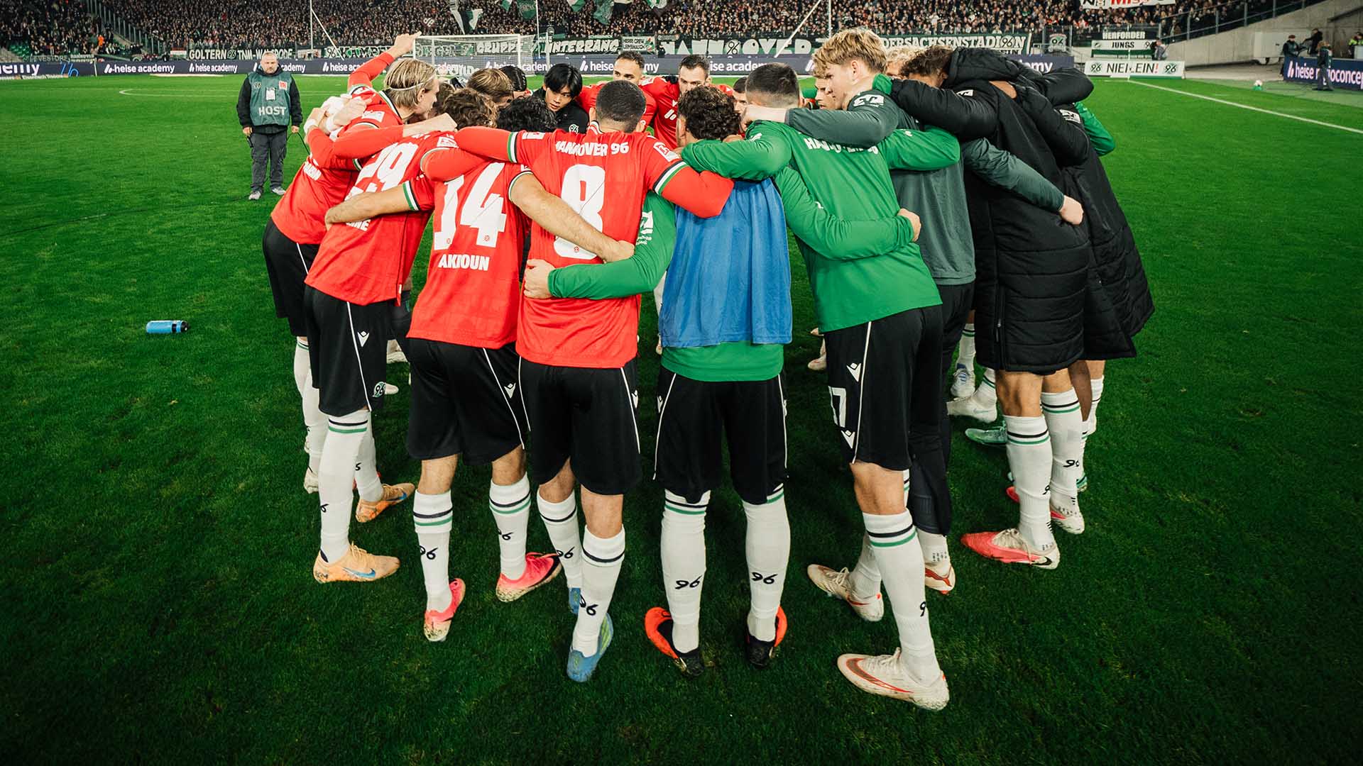 Die 96-Mannschaft bildet einen Kreis bei einem Heimspiel, Fans sind im Hintergrund zu sehen.