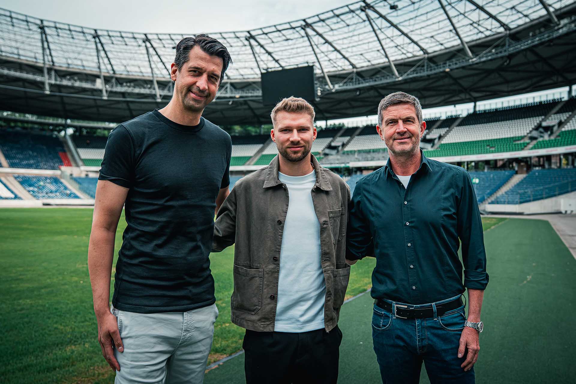 Jonas Boldt, Clemens Döring und Ralf Becker stehen im leeren Stadion, im Hintergrund die neuen schwarz-weiß-grünen Sitze.