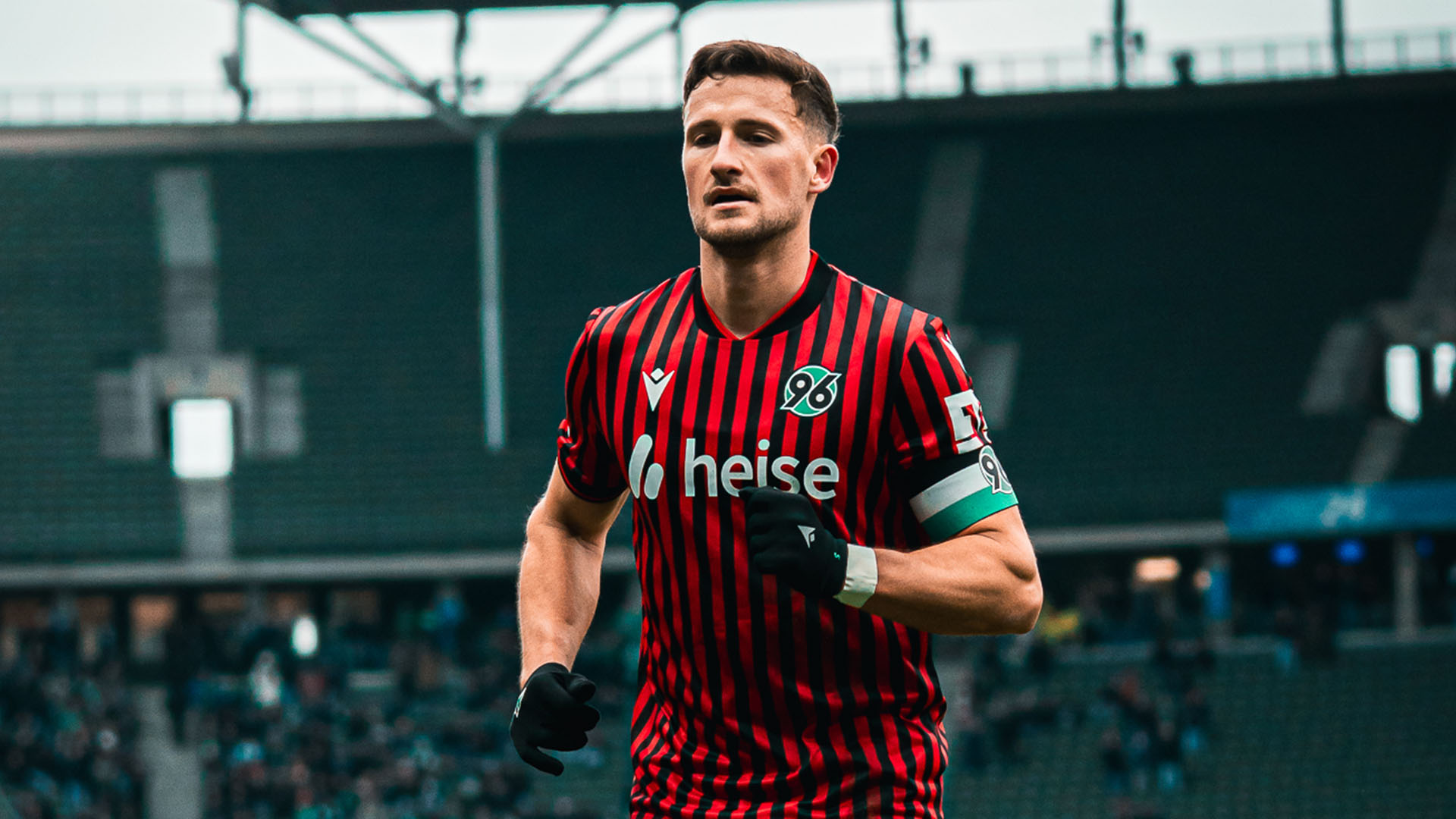Enzo Leopold trägt Handschuhe und läuft im rot-schwarz gestreiftem Trikot über den Rasen. Im Hintergrund sind die Ränge des Olympiastadions zu sehen.