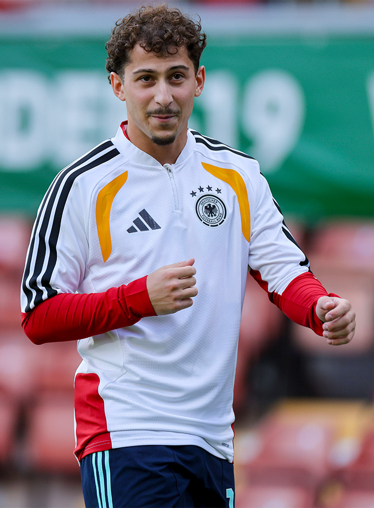 Der neue Spieler Taycan Etcibasi lächelt in einer weißen DFB-Jacke.