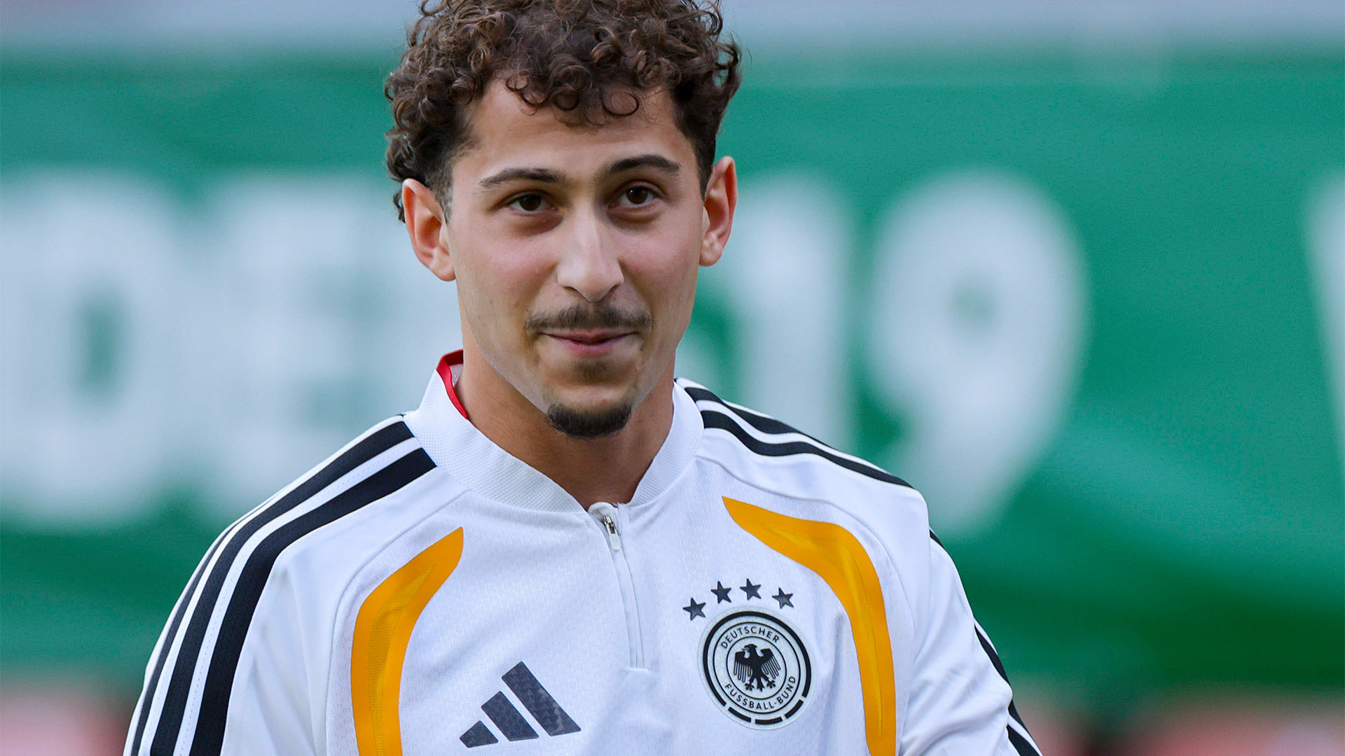 Der neue Spieler Taycan Etcibasi lächelt in einer weißen DFB-Jacke.