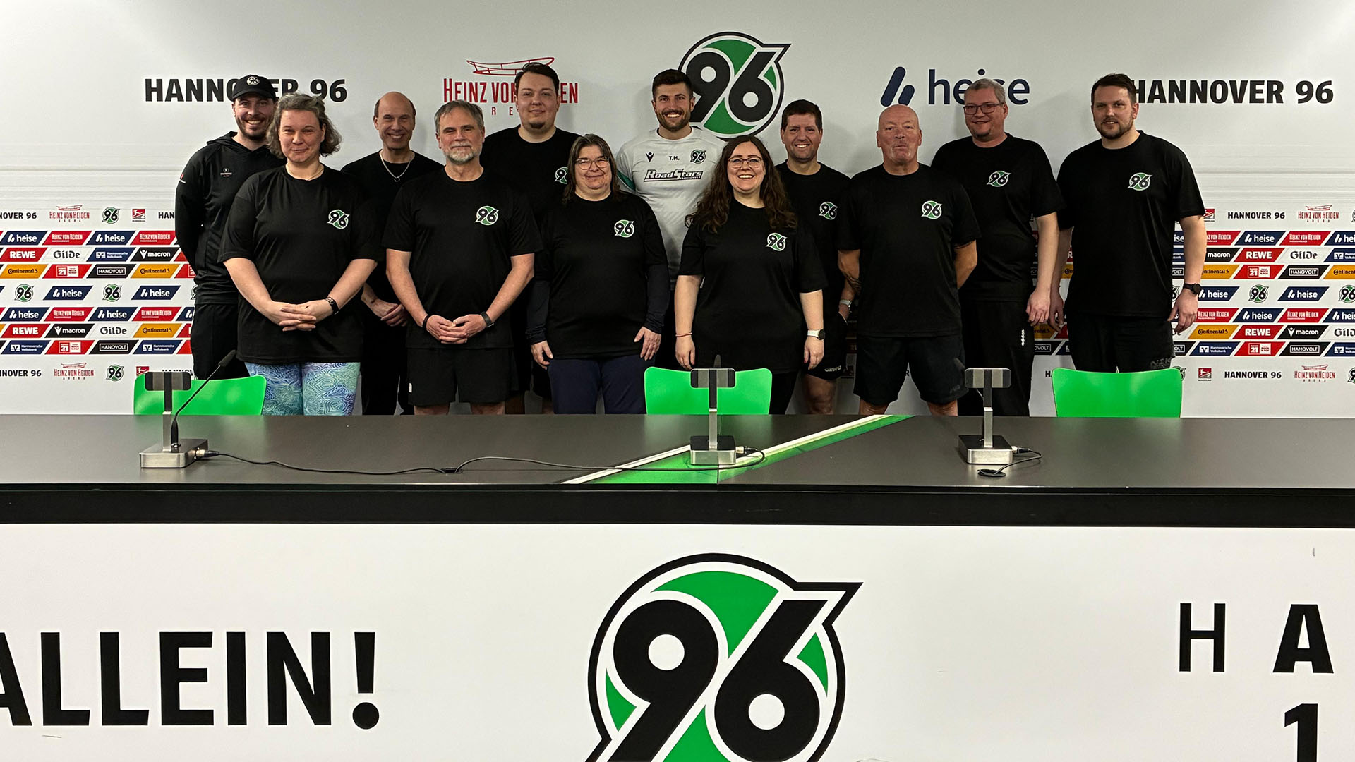 Eine Gruppe von Menschen in schwarze 96-T-Shirts steht auf dem Podium des Pressekonferenzraums. 