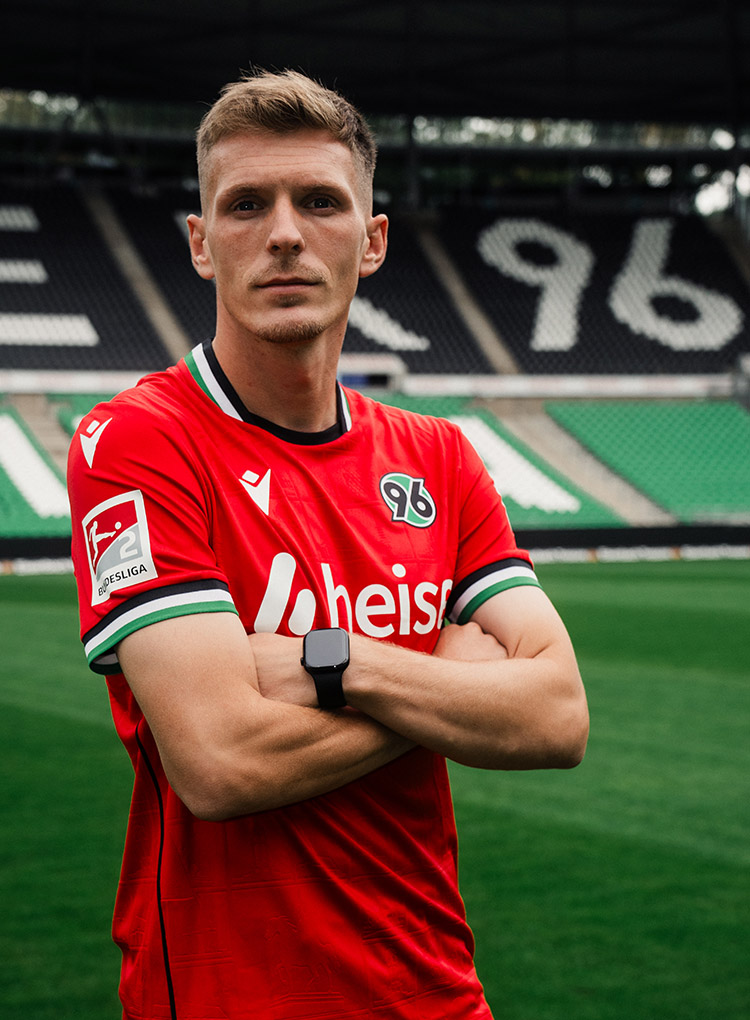 Der neue 96-Spieler Emir Sahiti steht im 96-Heimtrikot mit verschränkten Armen im Stadion.