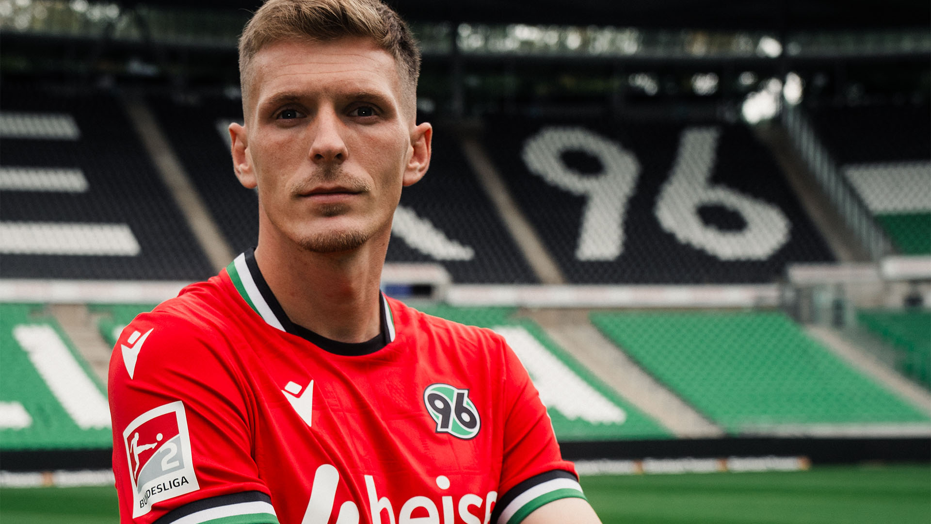 Der neue 96-Spieler Emir Sahiti steht im 96-Heimtrikot mit verschränkten Armen im Stadion.