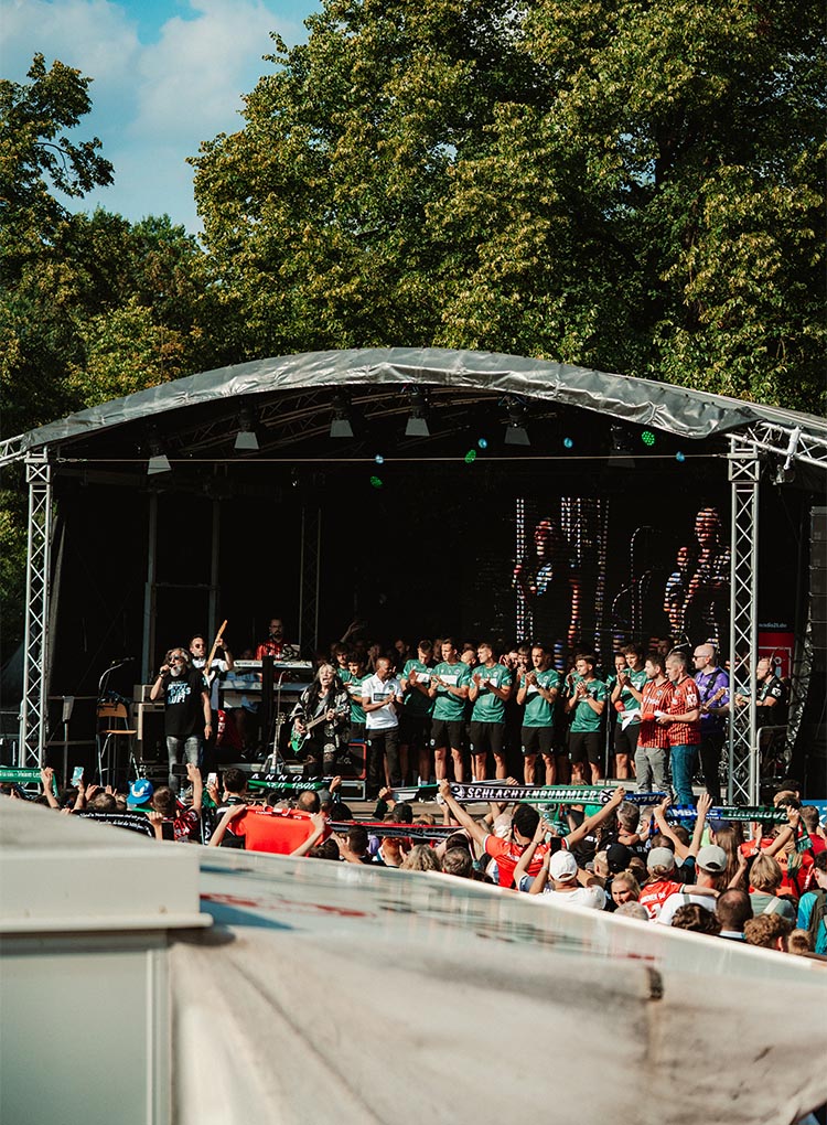 Die 96-Mannschaft steht auf der Bühne und singt mit Anca und Ossy, Fans davor schwenken Schals.