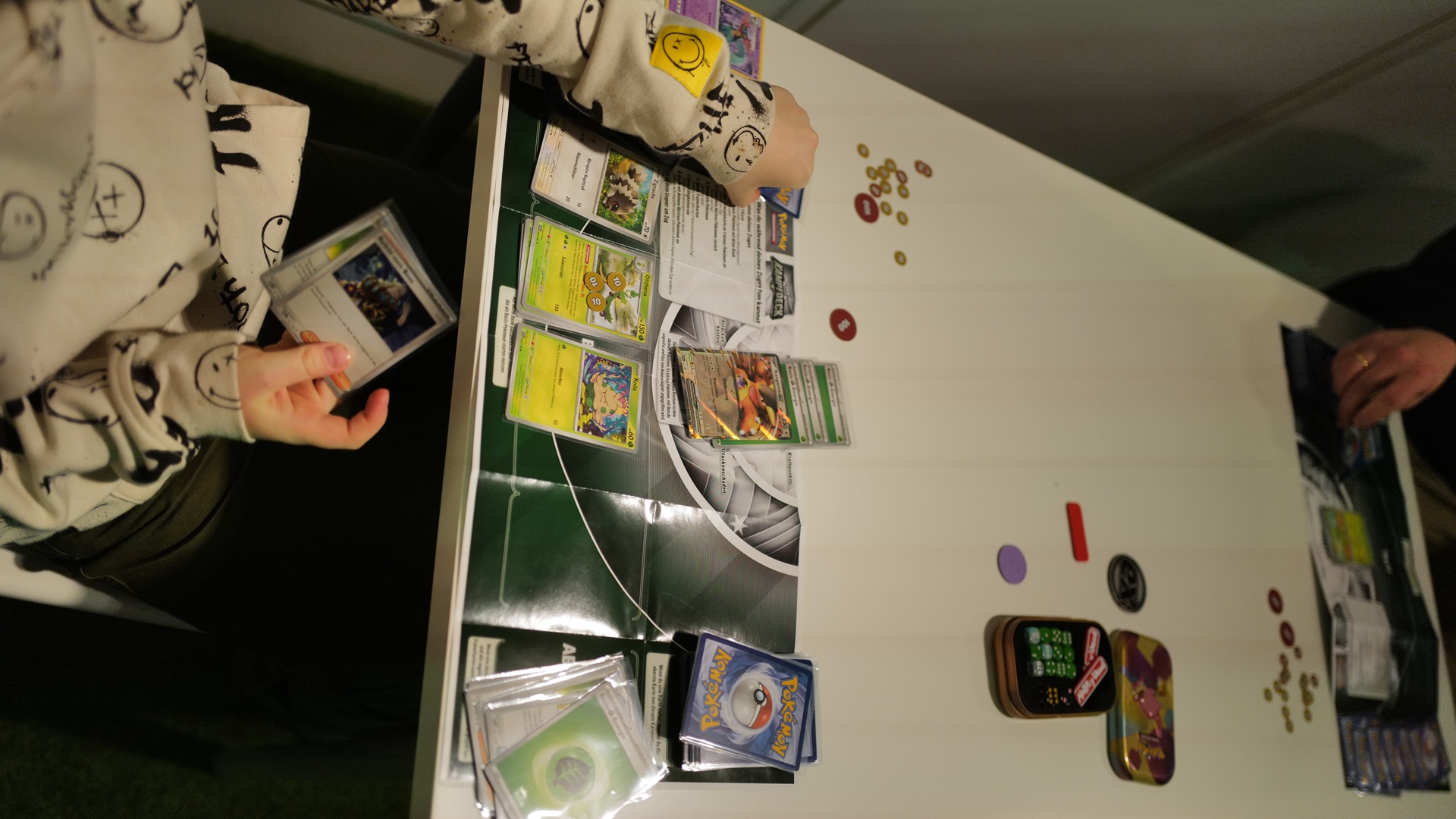 Kinder sitzen an einem Tisch mit mehreren Pokémon-Sammelkarten