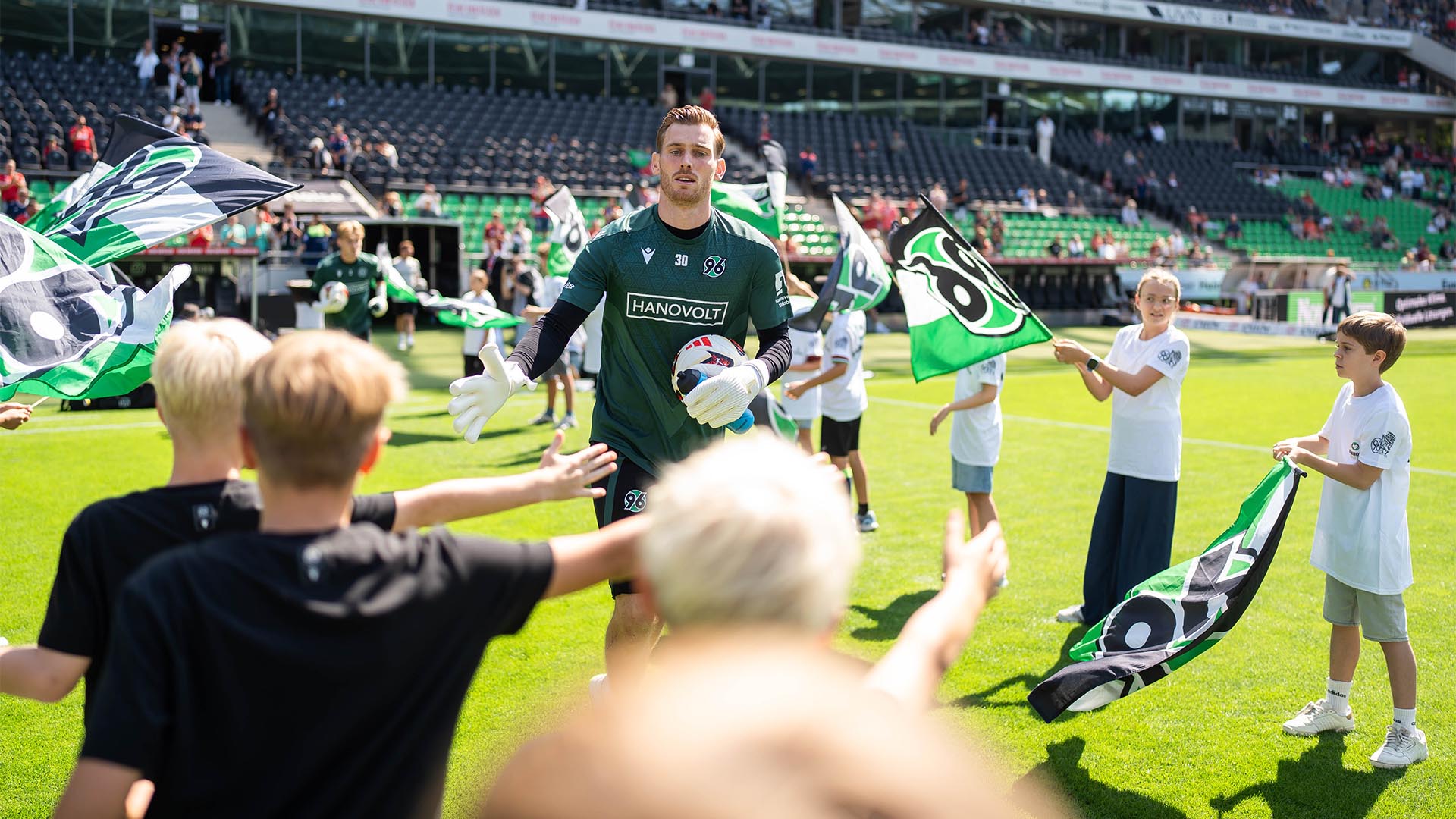 96-Spieler laufen zum Warmmachen ins Stadion und klatschen mit Kindern mit Fahnen ab.