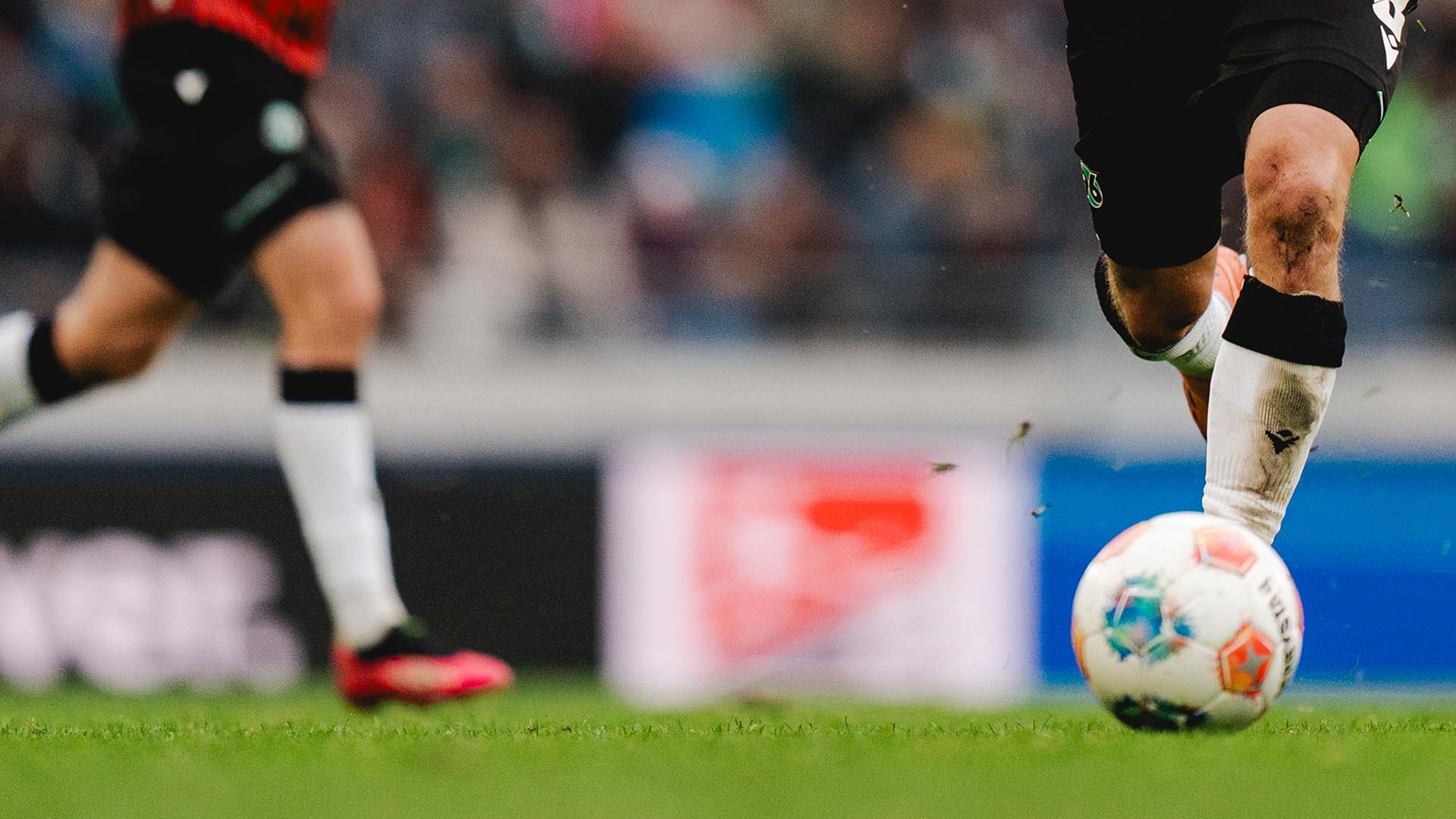 Ein laufender Spieler mit Ball am Fuß ist bis knapp übers Knie zu sehen.