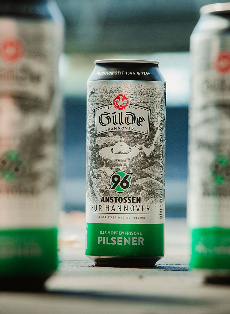 Eine neue Gilde-Dose ist scharf zu sehen, zwei andere im Vordergrund unscharf. Im Hintergrund ist unscharf das Stadion.
