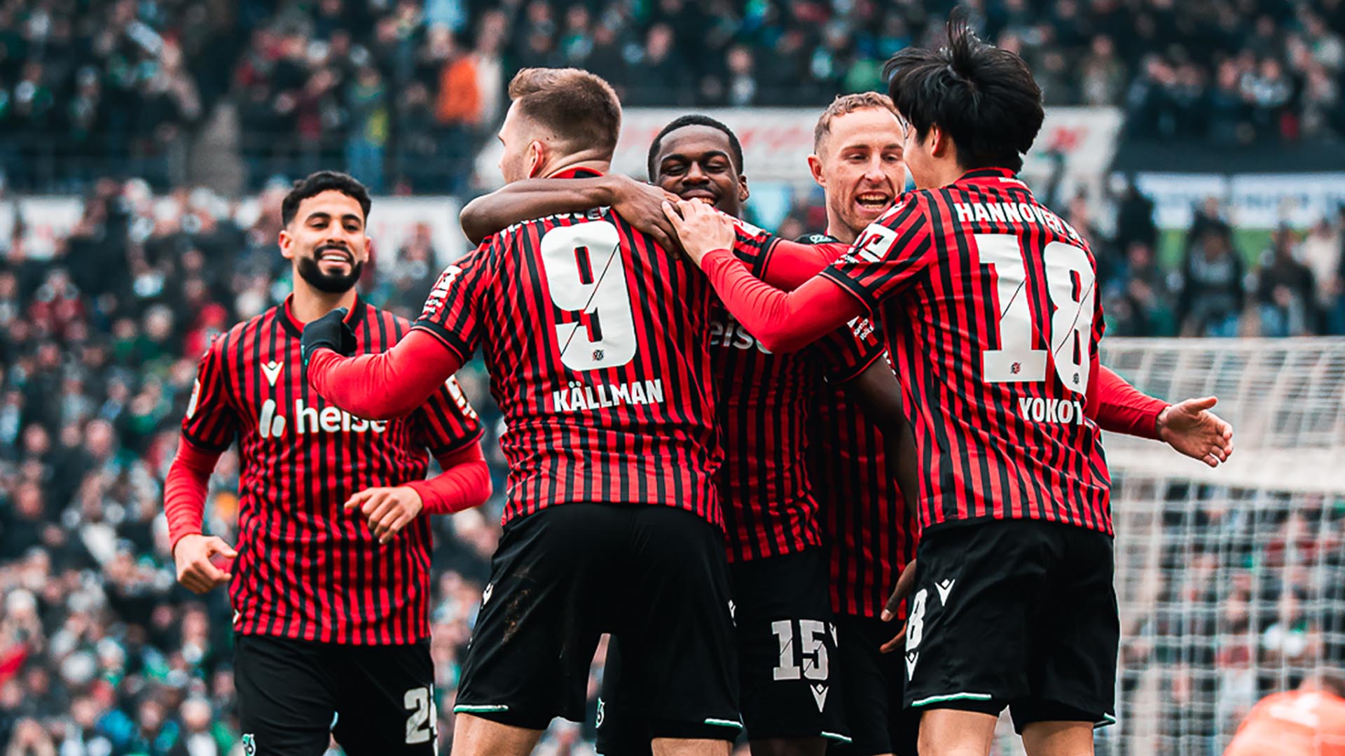 Eine Traube 96-Spieler jubelt im Heimtrikot vor Fans im Hintergrund.