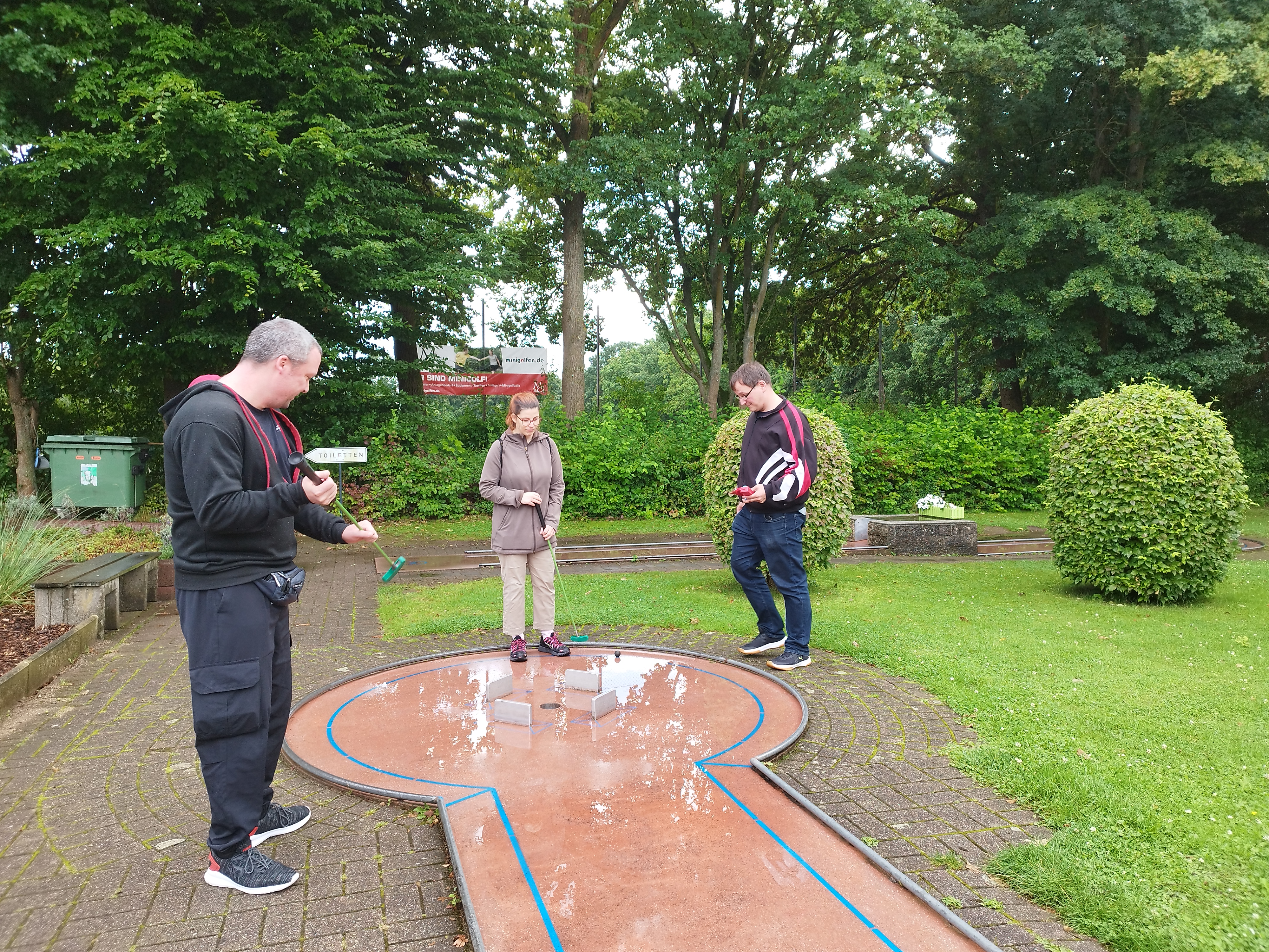 Drei Personen beim Minigolf spielen.