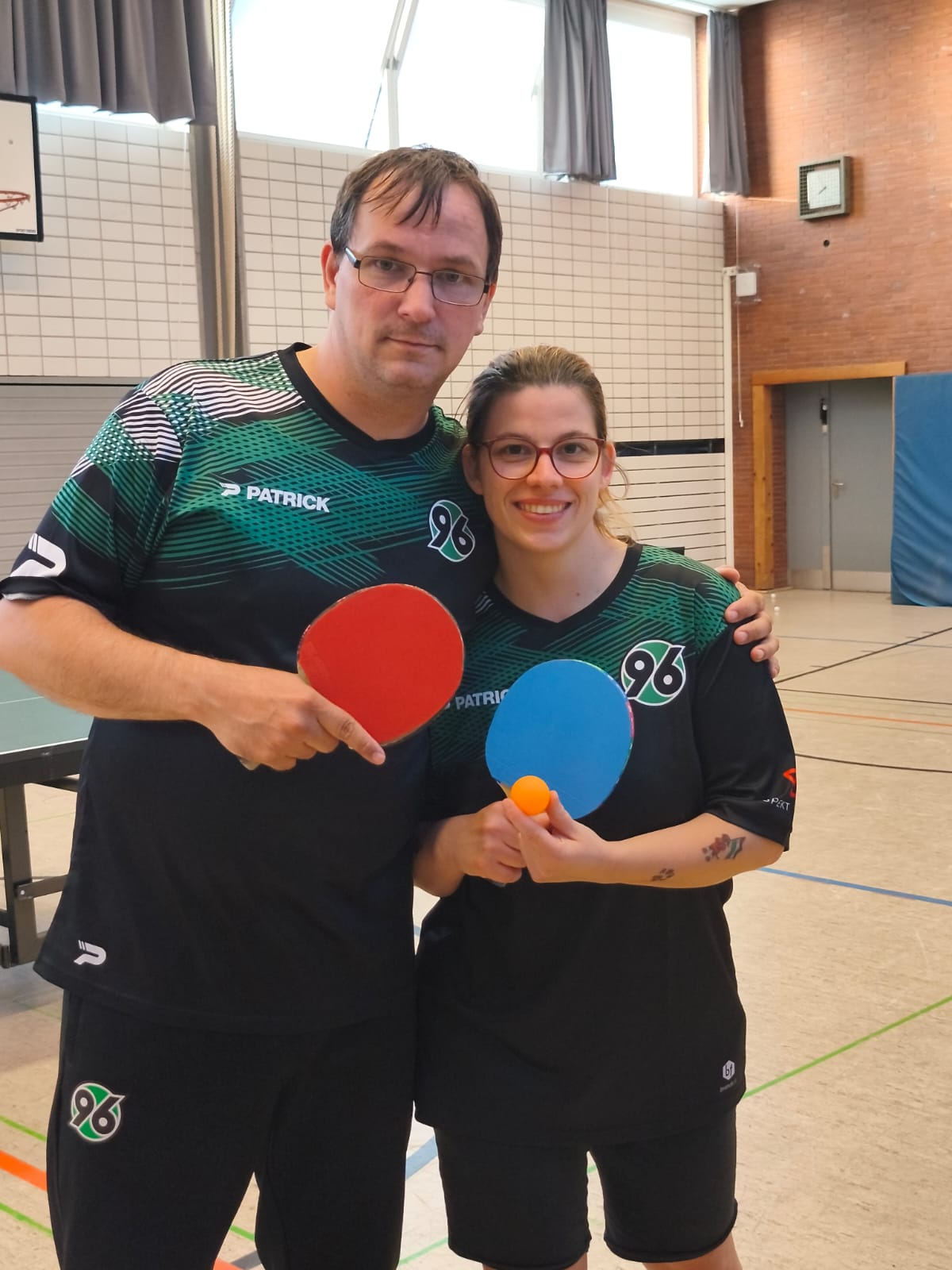 Norman Lindner und Franzsika Sieber aus der Abteilung Handicapsport von Hannover 96 in Trikots und mit Tischtennis-Schlägern