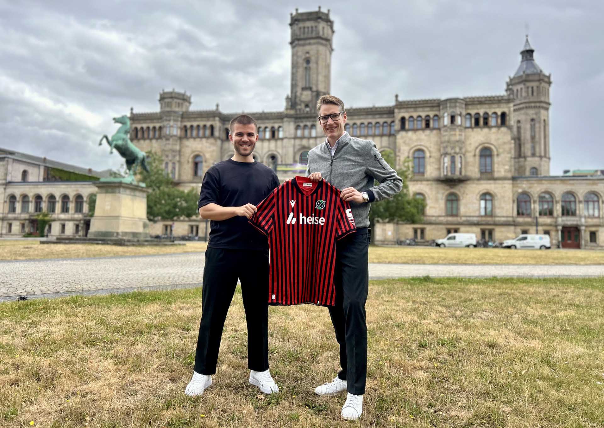 Arian Ahlers und Henning Bindzus halten gemeinsam ein 96-Heimtrikot, im Hintergrund die Leibniz Universität.