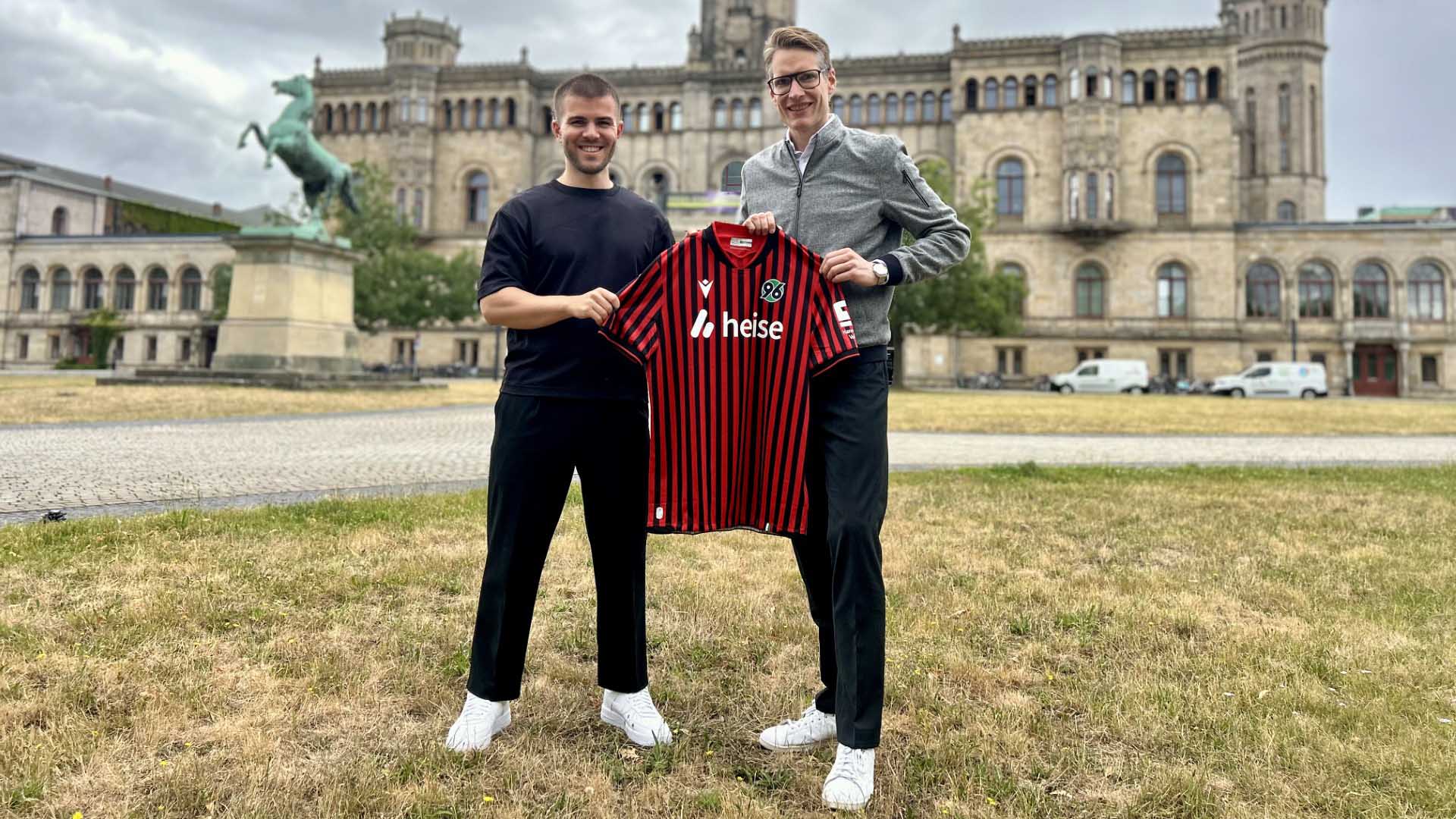 Arian Ahlers und Henning Bindzus halten gemeinsam ein 96-Heimtrikot, im Hintergrund die Leibniz Universität.
