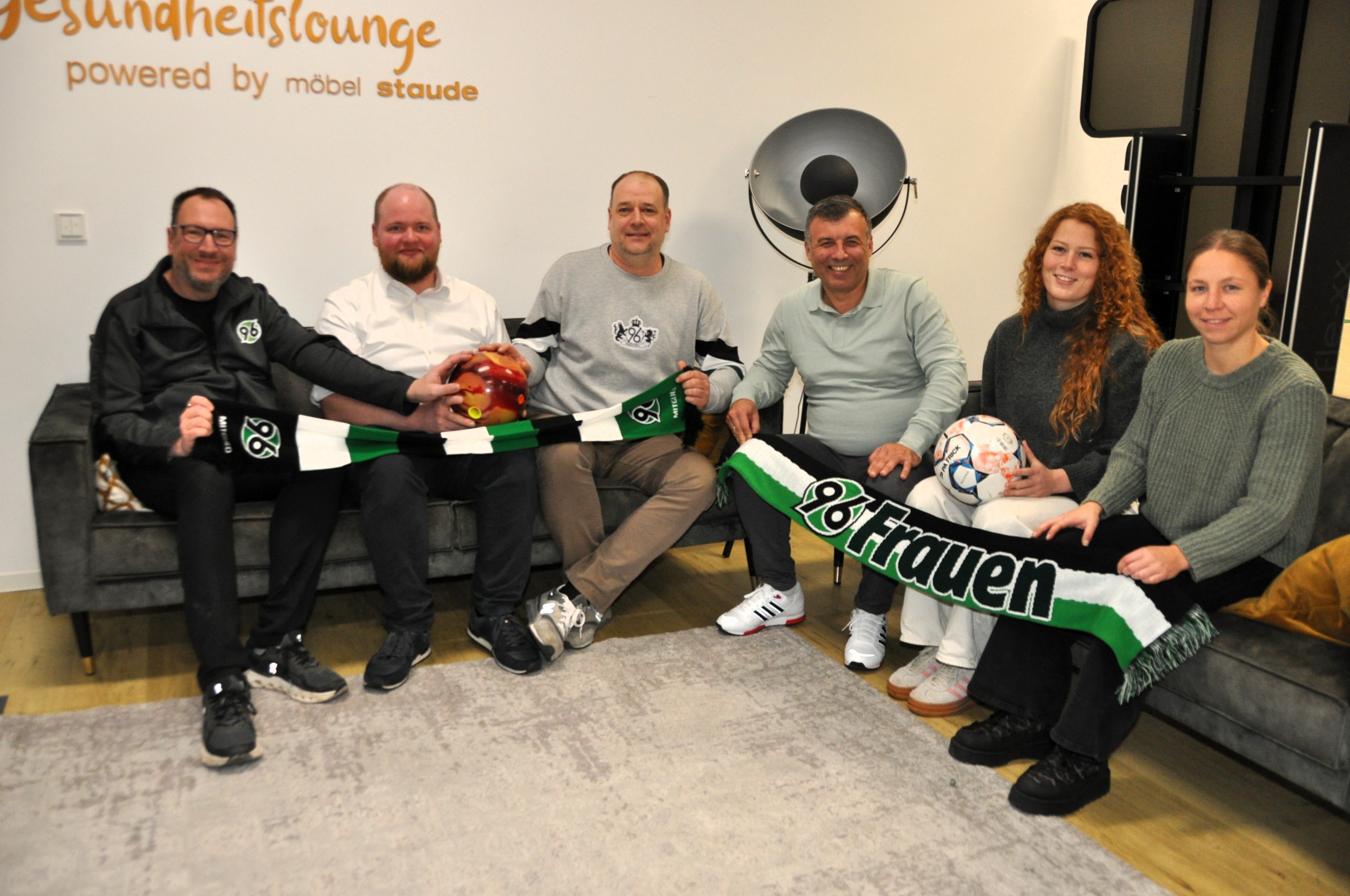 Sechs Personen sitzen auf einem Sofa und lächeln in die Kamera.