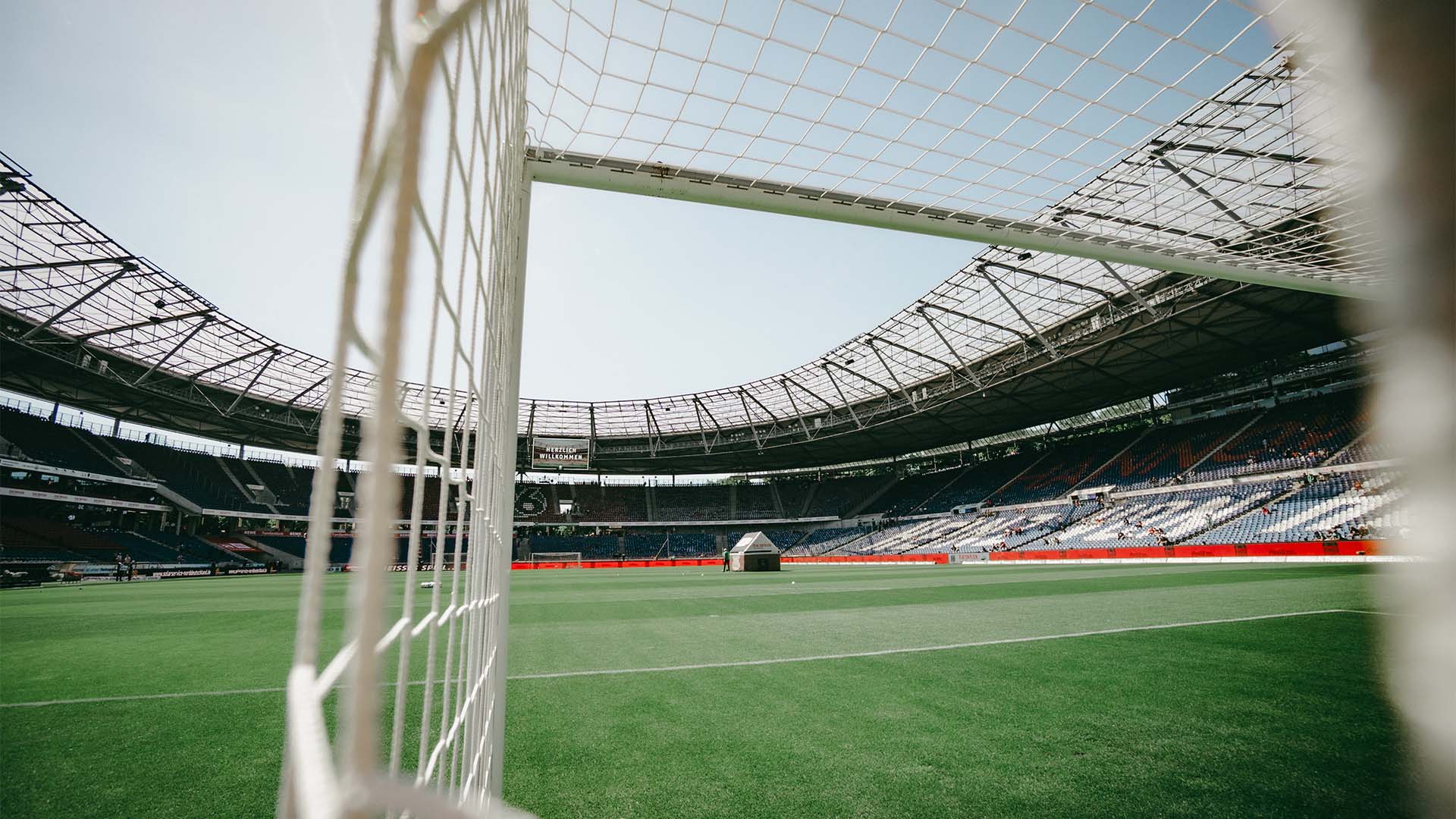 Die fast leere Heinz von Heiden Arena bei Sonne, im Vordergrund unscharf ein Tornetz.