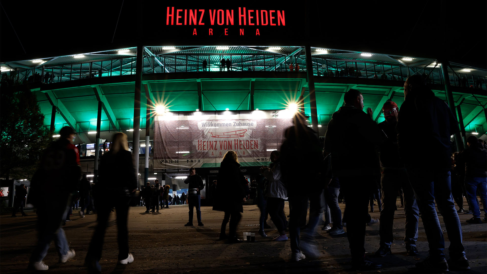 Blick auf den hell erleuchteten Eingang der Heinz von Heiden Arena, Menschen gehen ins Stadion.