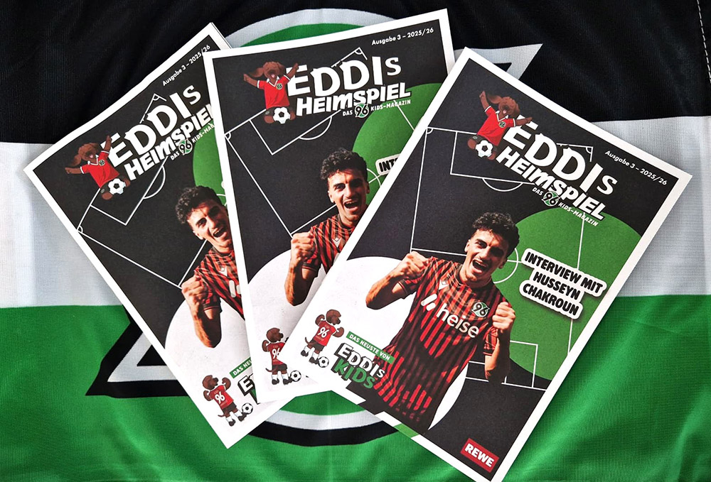Drei neue Heimspielmagazine mit Husseyn Chakroun auf dem Cover liegen auf einer 96-Fahne.