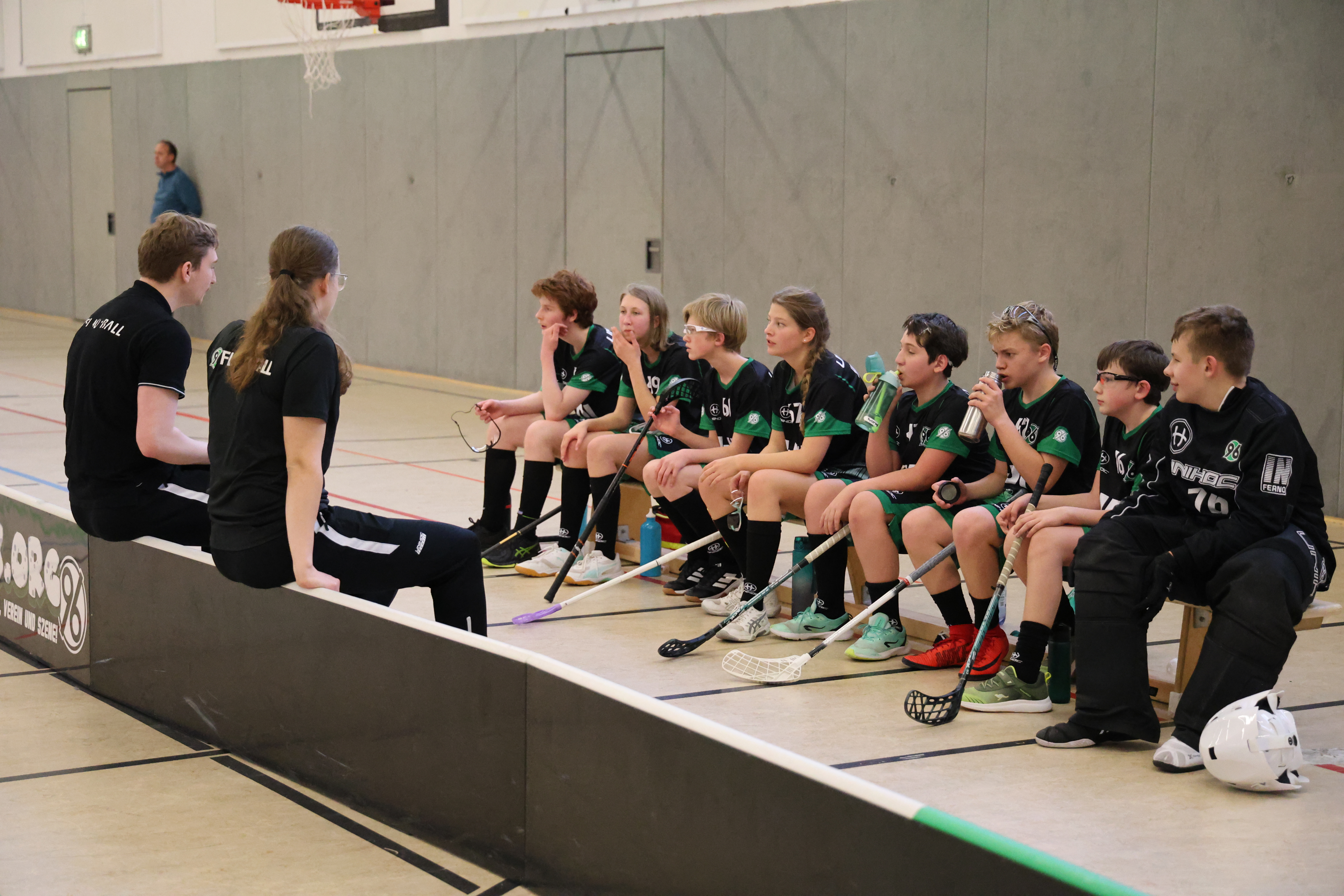 Die SpielerInnen sitzen auf einer Bank und hören den TrainerInnen zu.
