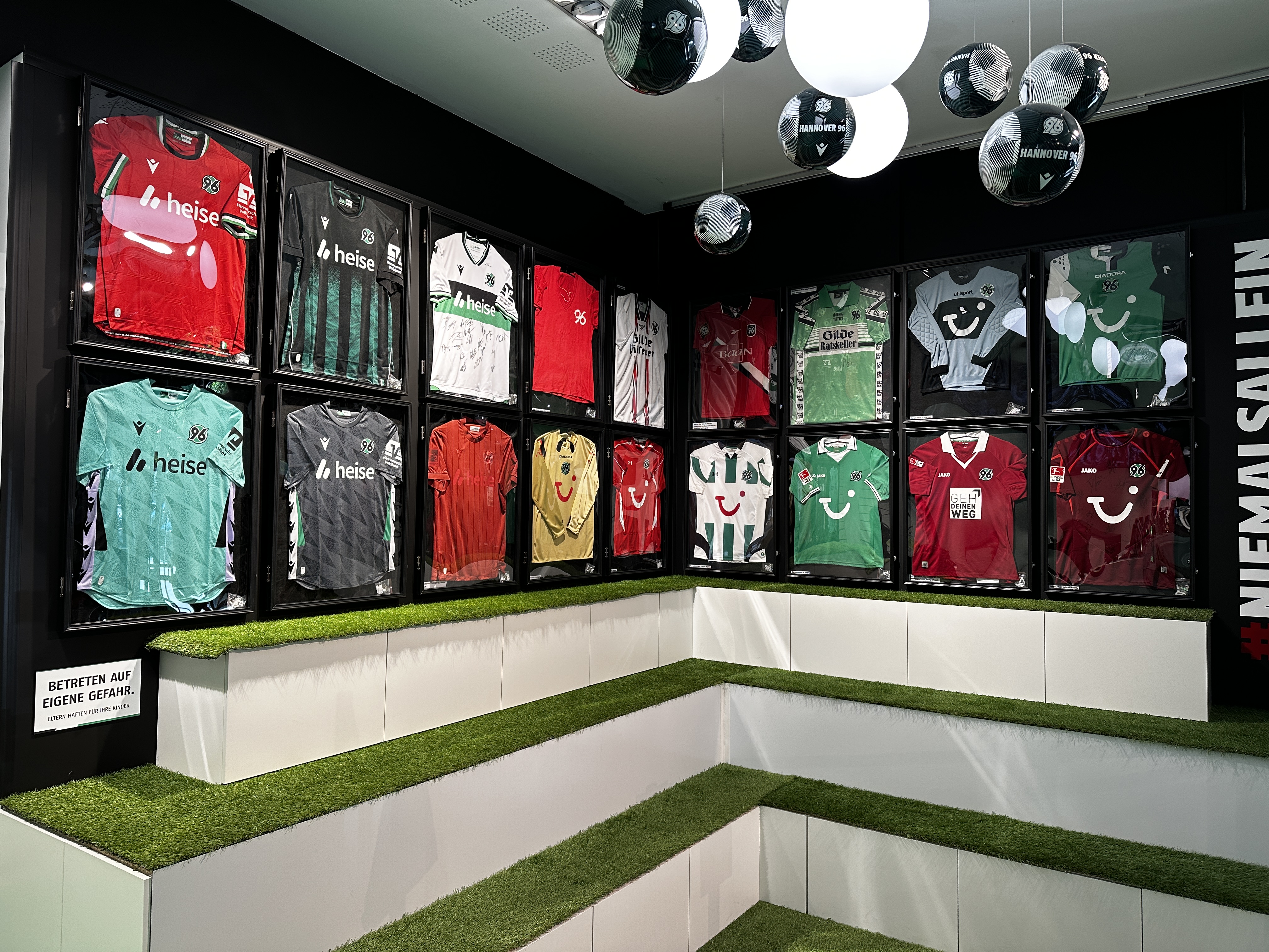 Die aktuellen Hannover 96 Trikots sowie aus der Vergangenheit hängen in Bilderrahmen an einer Wand.