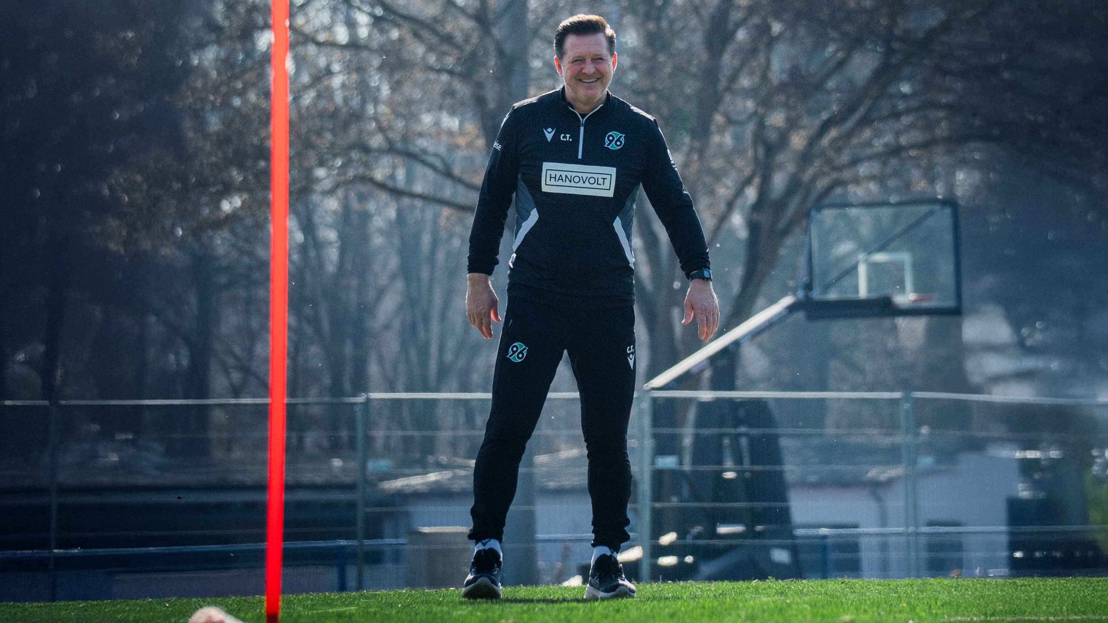 Der Trainer steht auf dem Trainingsplatz und lächelt.