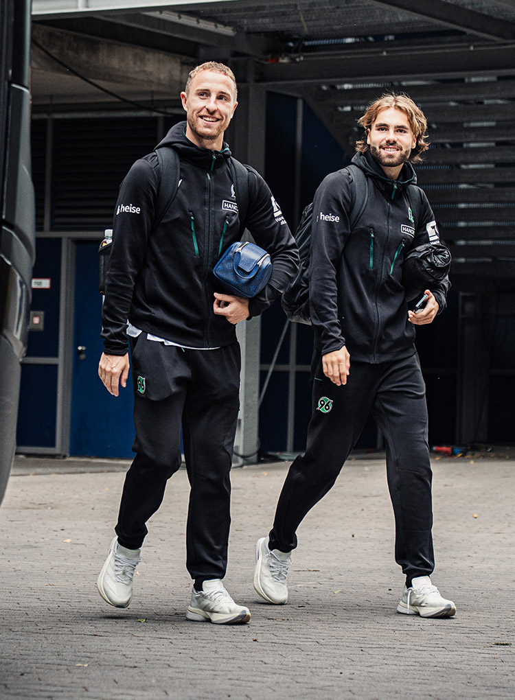 Die 96-Spieler Maurice Neubauer und Kolja Oudenne laufen in schwarzer 96-Kleidung nebeneinander, beide lächeln.