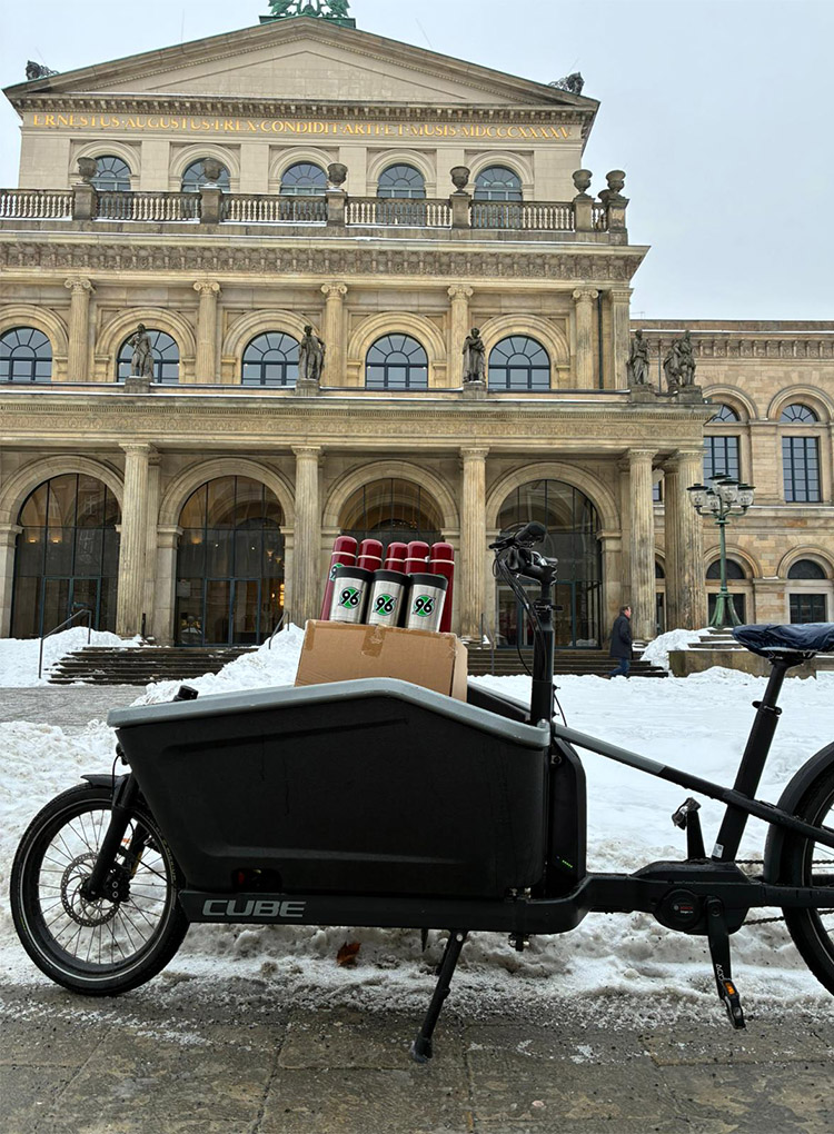 Ein mit Thermosbechern beladenes Lastenfahrrad steht vor der Oper in Hannover, es liegt Schnee.