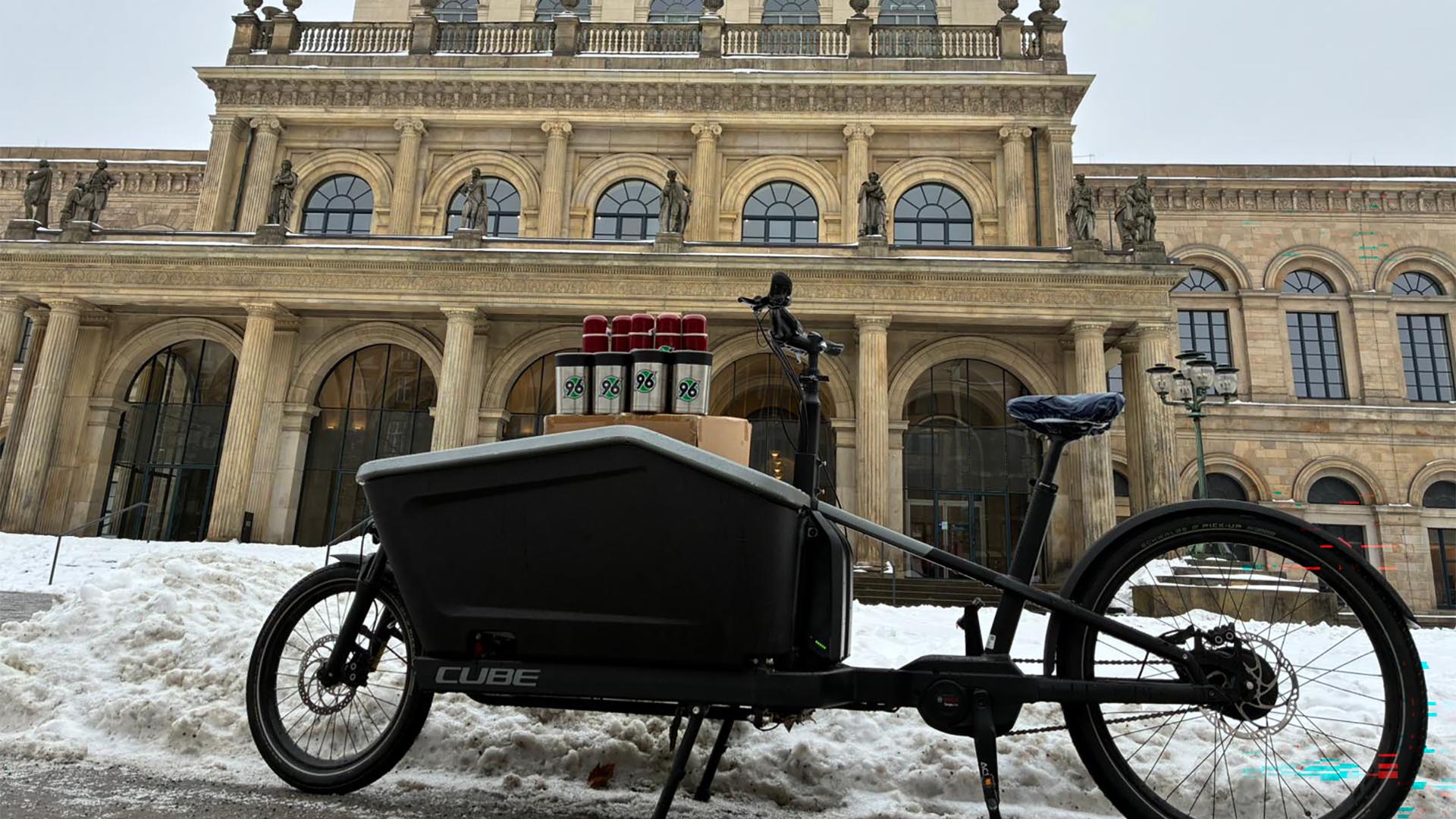 Ein mit Thermosbechern beladenes Lastenfahrrad steht vor der Oper in Hannover, es liegt Schnee.