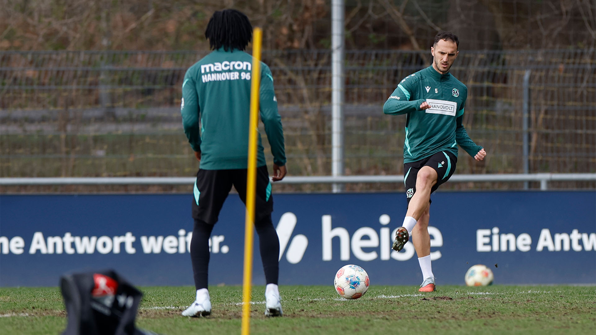 Vigil Ghita passt einen Ball auf dem Trainingsplatz, Hendry Blank ist von hinten zu sehen. 