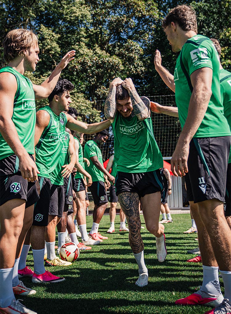 Der 96-Spieler Marcel Hartel läuft auf dem Trainingsplatz durch ein Spalier von anderen Spielern und hält sich die Hände über den Kopf.