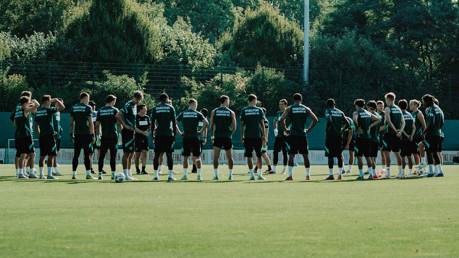 Die 96-Mannschaft steht bei Sonnenschein im Kreis auf dem Trainingsplatz. 
