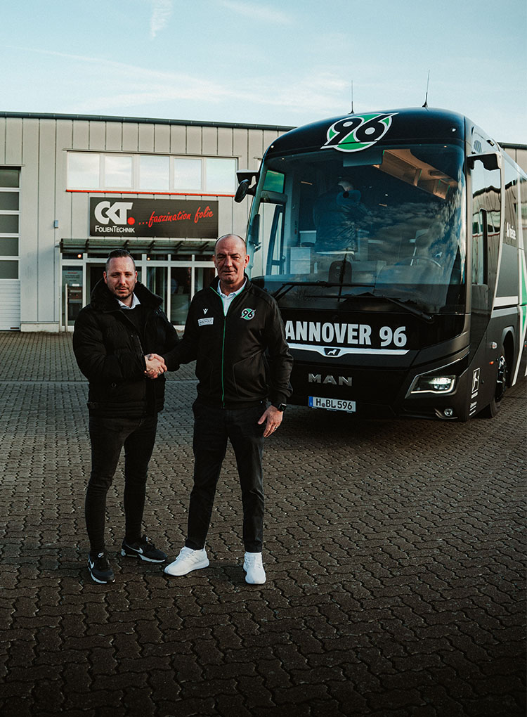 Zwei Personen stehen vor dem Bus und machen einen Handshake.