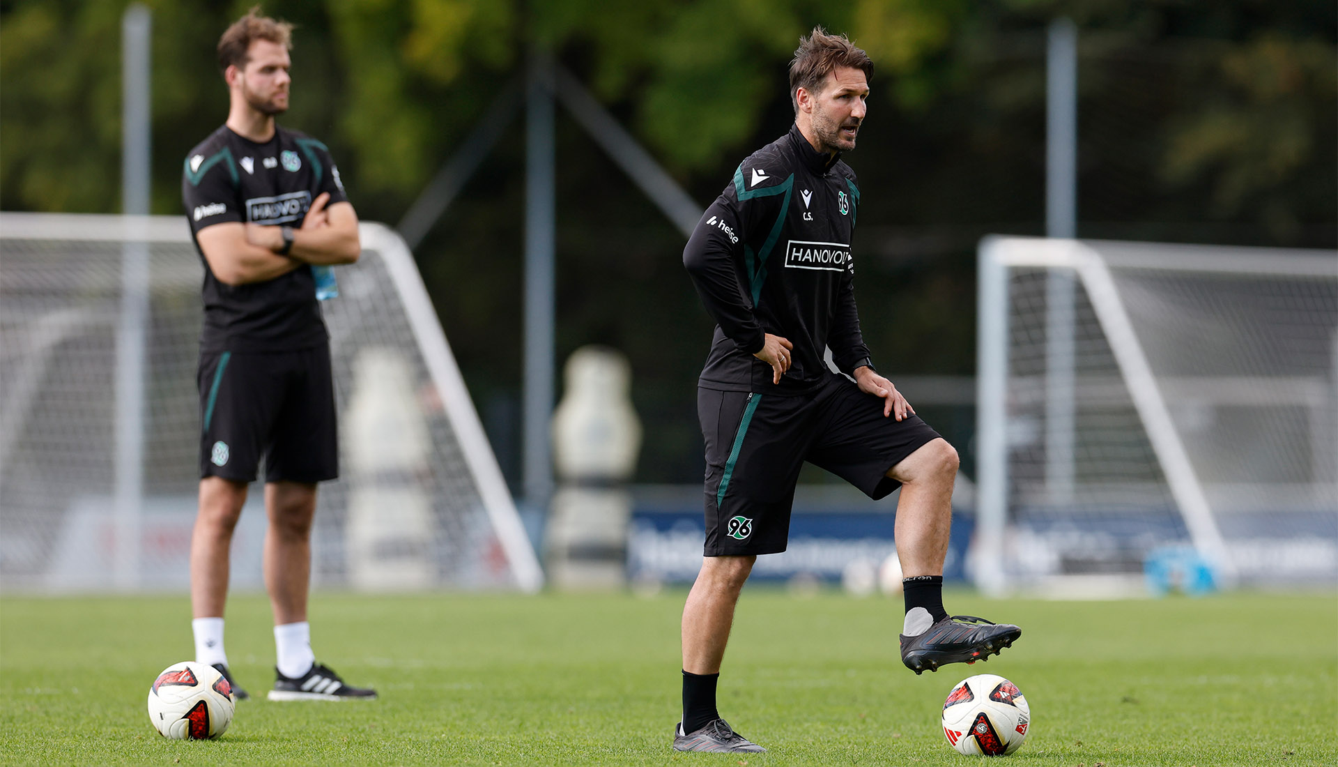 Der 96-Co-Trainer Christian Schulz steht auf dem Trainingsplatz und hat einen Fuß auf dem Ball.