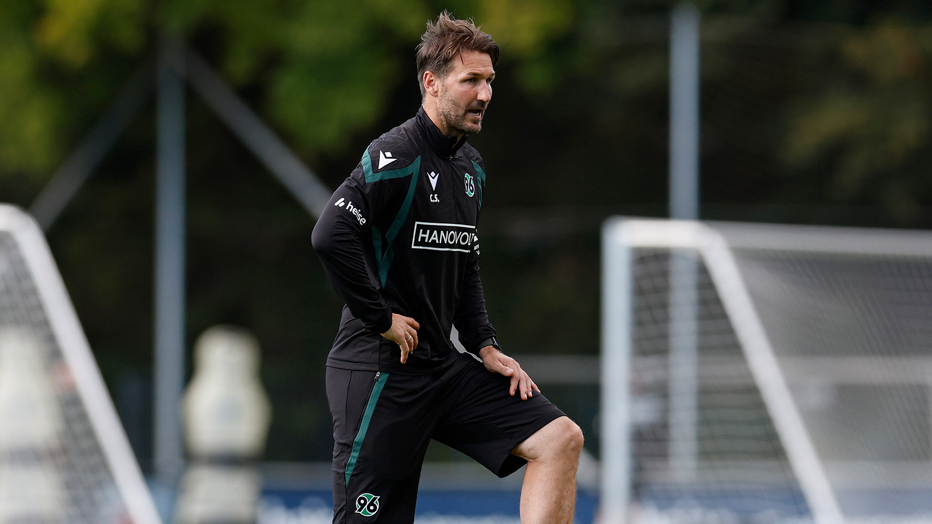 Der 96-Co-Trainer Christian Schulz steht auf dem Trainingsplatz und hat einen Fuß auf dem Ball.