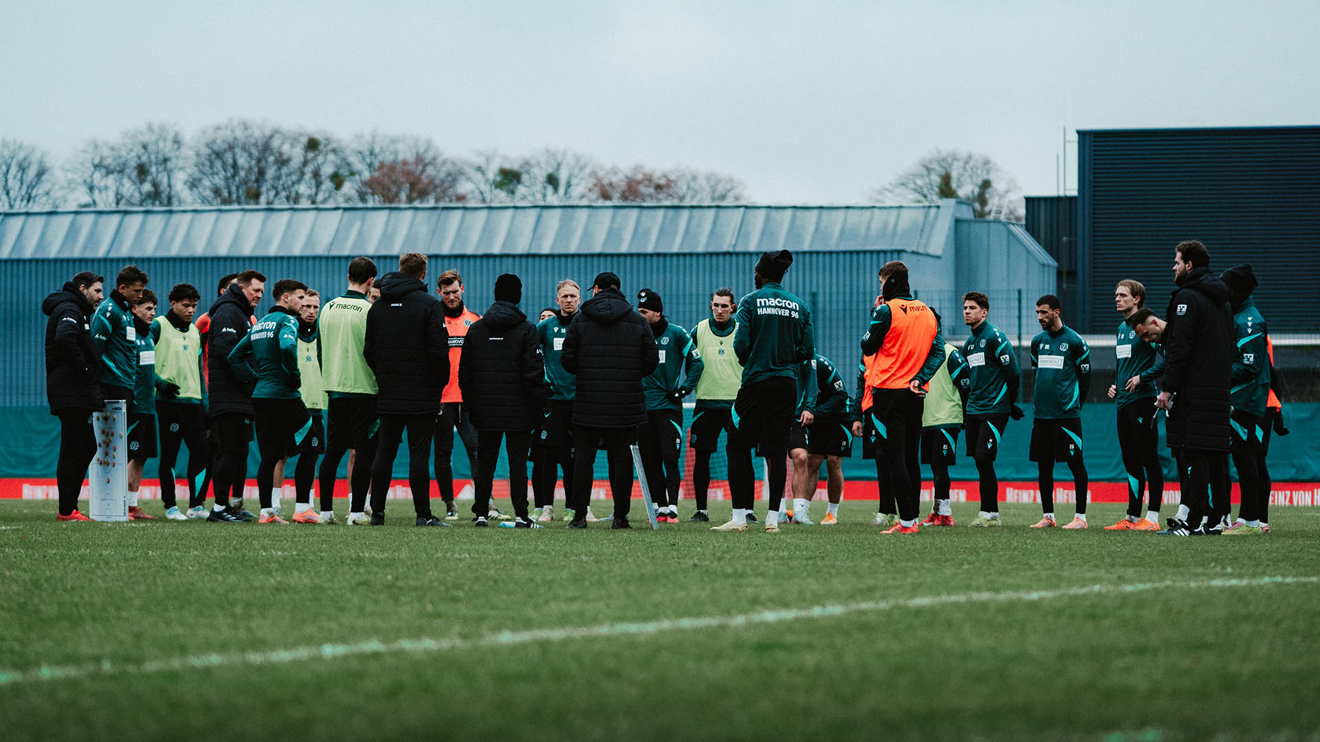 Die 96-Mannschaft steht in einem Kreis auf dem Trainingsplatz, der Himmel ist grau.